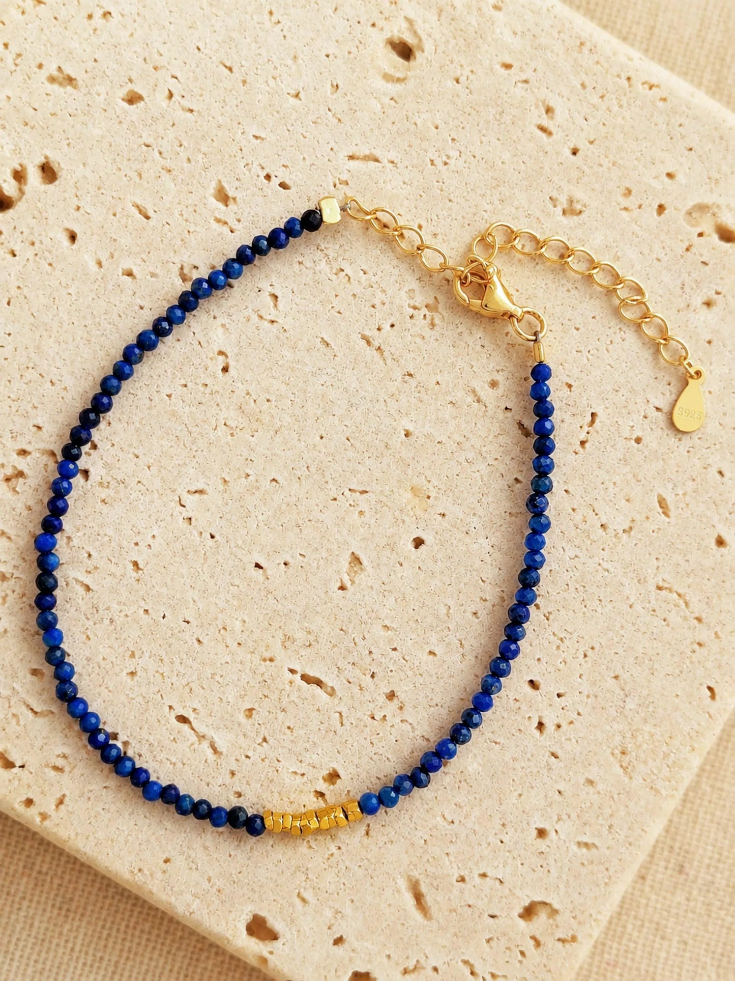 A beaded 18k gold vermeil bracelet featuring faceted lapis lazuli gemstone in deep blue color displayed on an aesthetic beige color stone, delicate and minimal style for everyday wear.