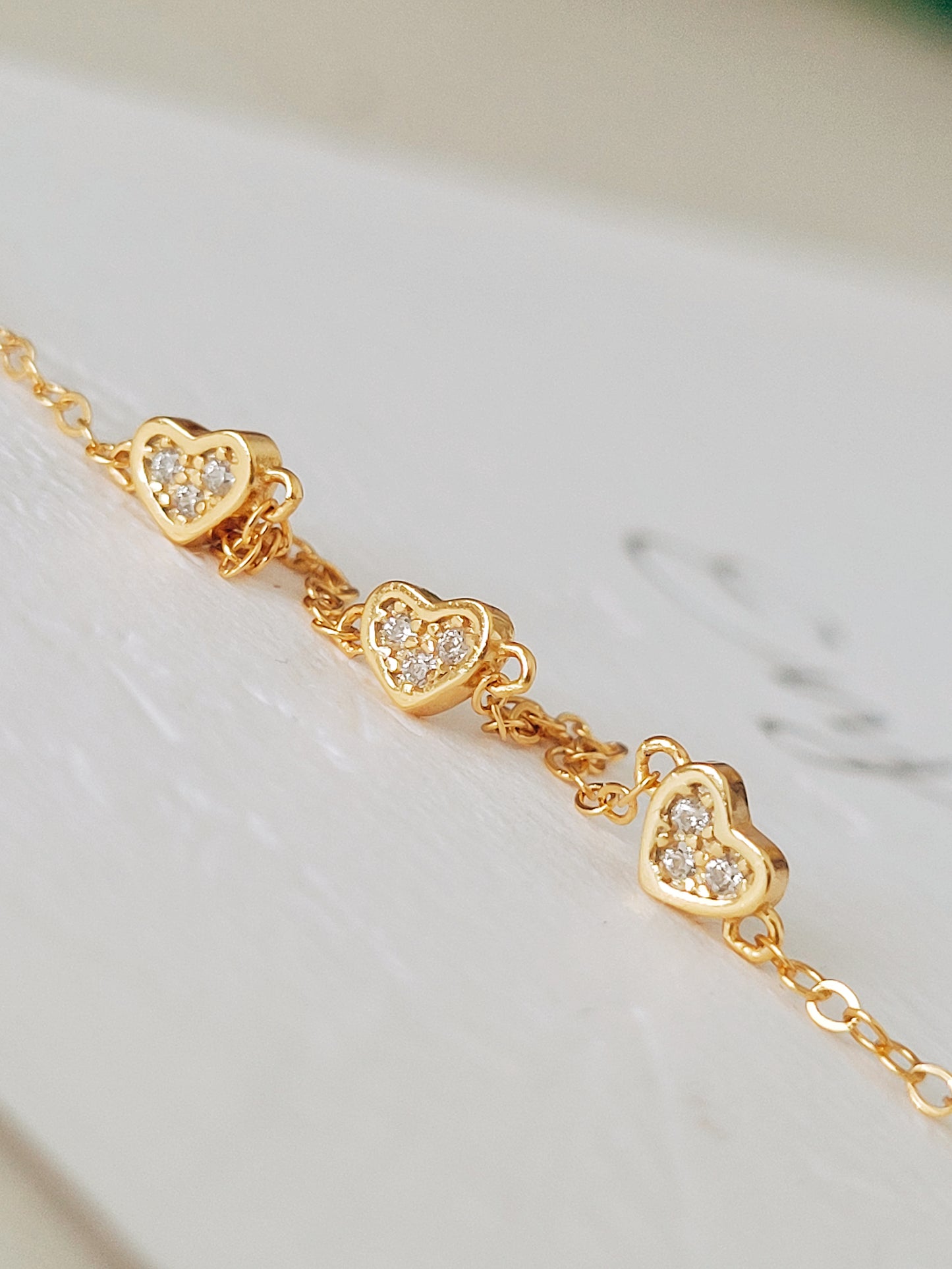 Close up of mini heart bracelet showing the details of the heart charm crafted in 14ct gold plated on 925 sterling silver with zirconia stones.