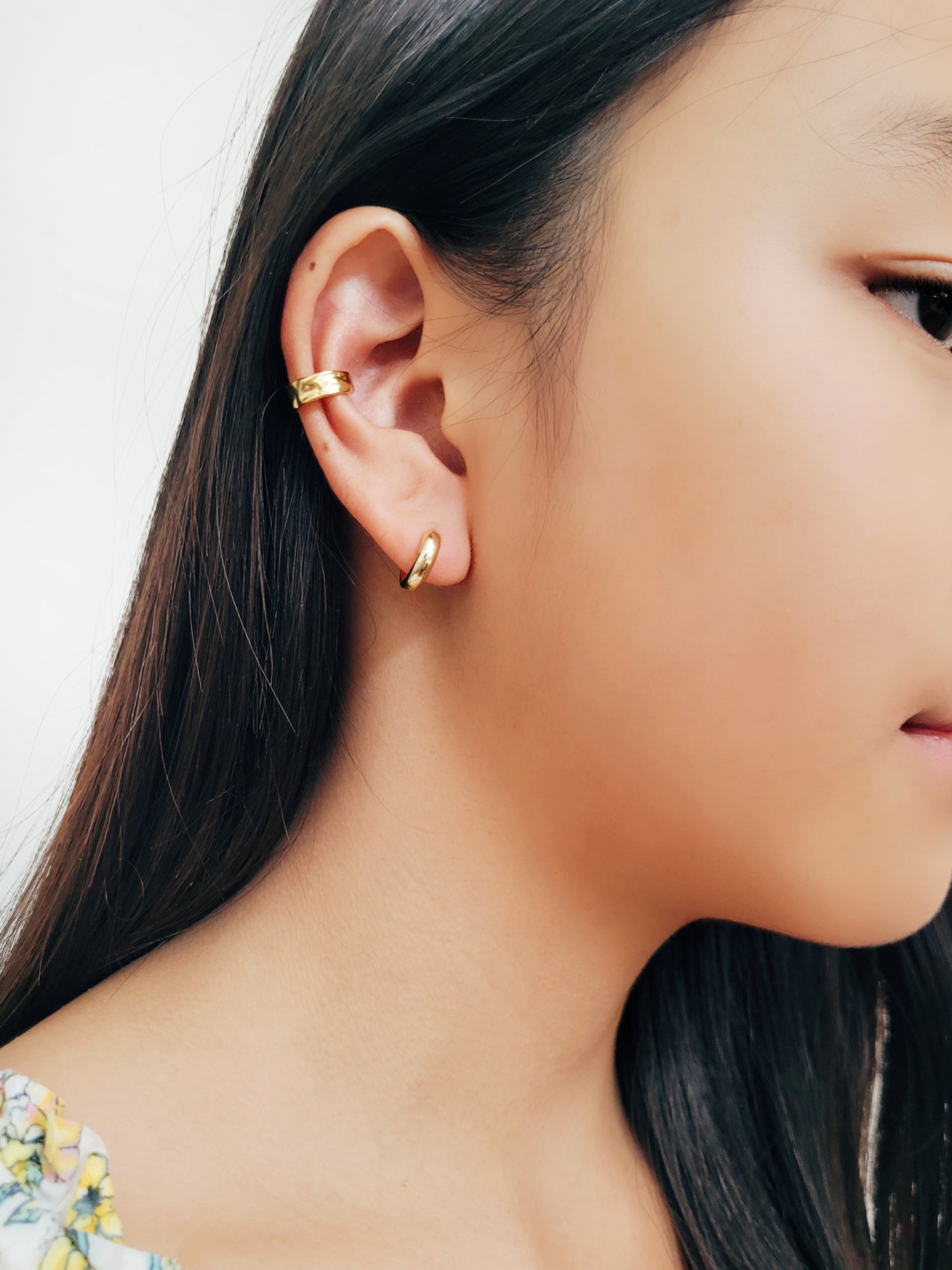 A girl wearing a textured gold ear cuff earring match with a sleek small gold hoop, dainty and minimalist style