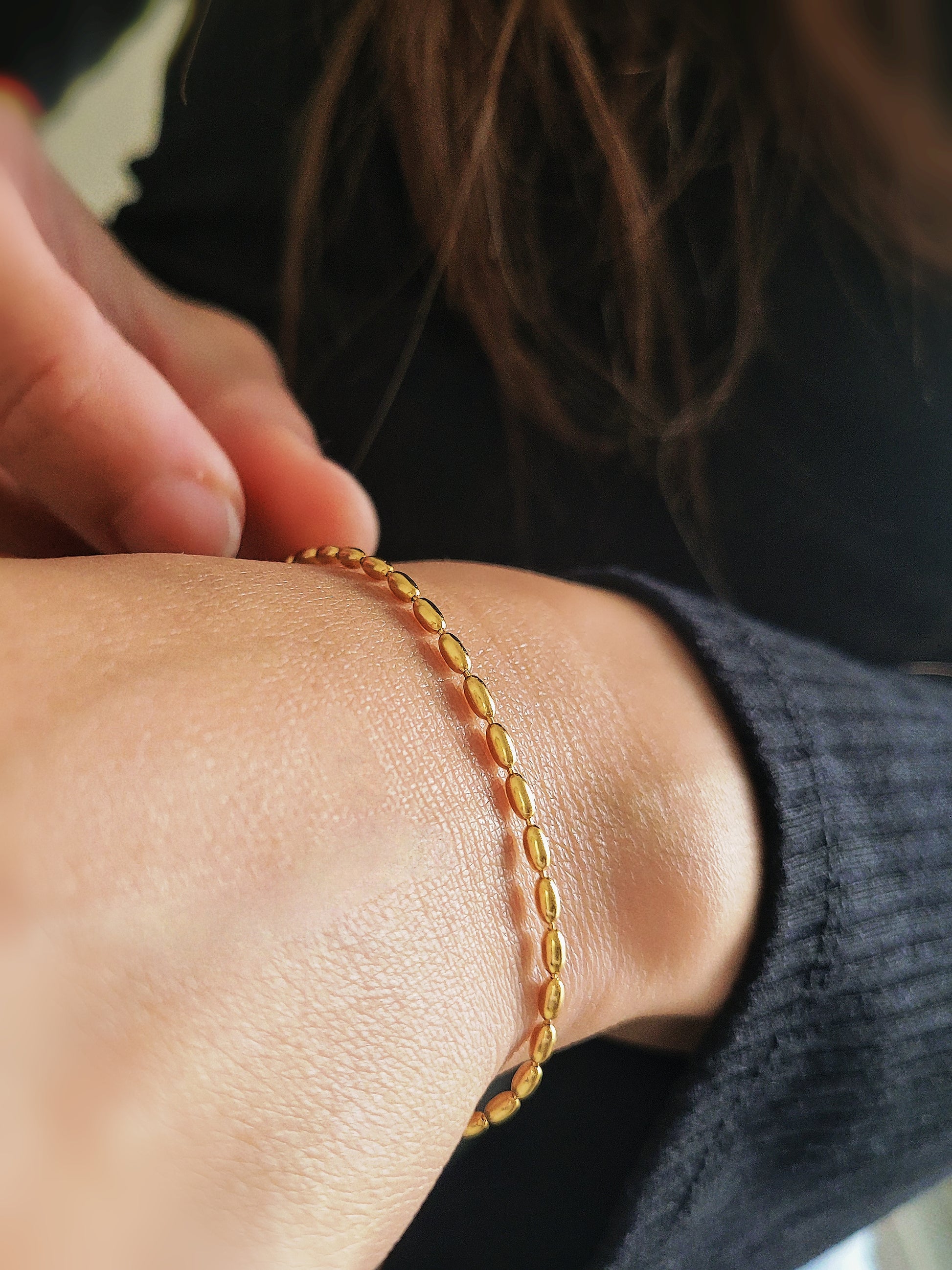 Close-up of a woman's hand wearing the elegant and dainty gold-plated oval beaded bracelet, highlighting its lustrous finish and intricate bead arrangement.