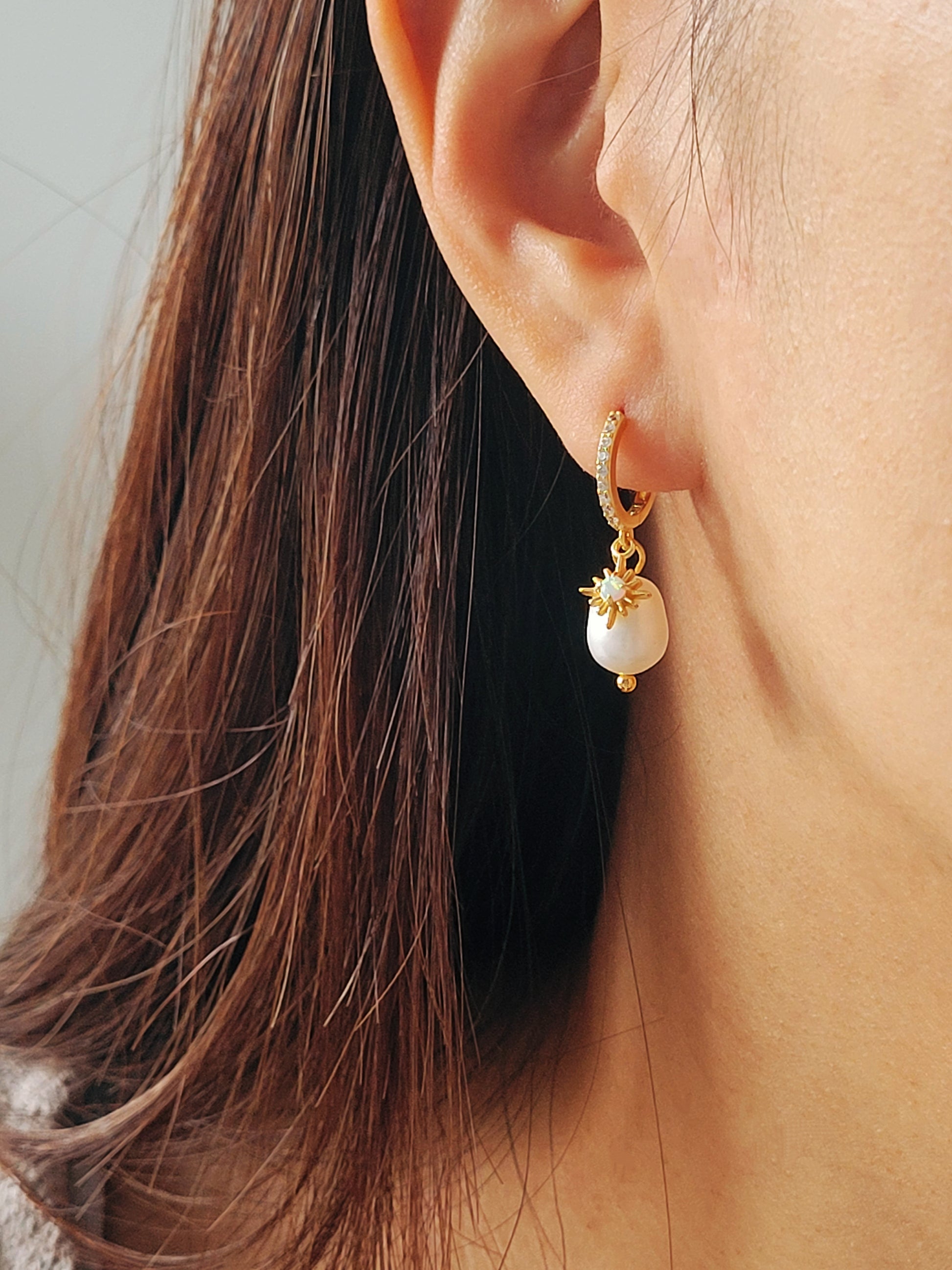 Woman wearing dainty freshwater pearl drop gold huggie earring featuring opal gemstone charm, crafted in gold plated sterling silver. Perfect bridal or everyday earrings with celestial charm and timeless sophistication. Anniversary gift for her.