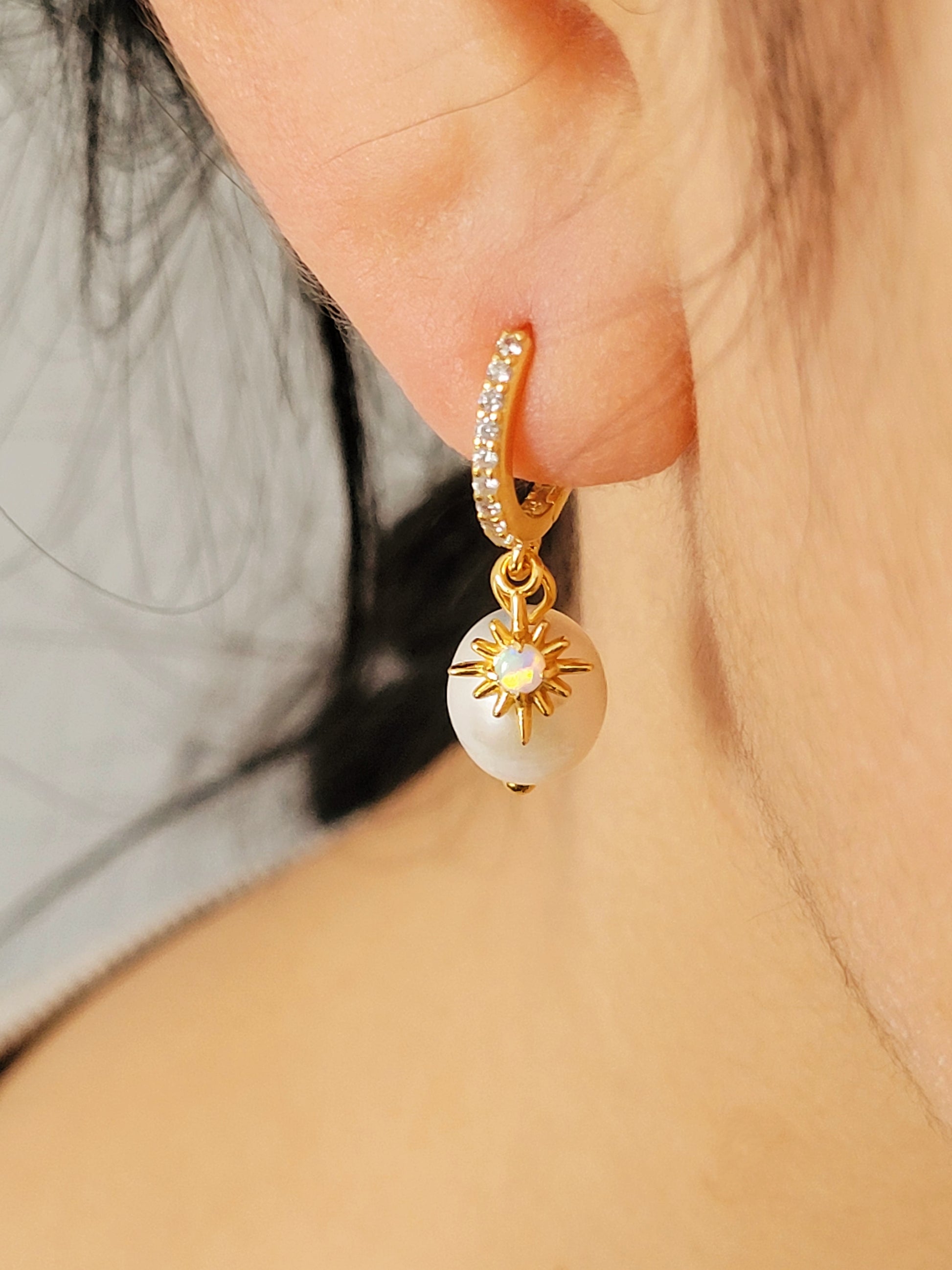 Woman wearing dainty freshwater pearl drop earring featuring a gold opal charm, crafted in gold plated sterling silver. Perfect bridal or everyday earrings with celestial charm and timeless sophistication. Birthday gift for her.