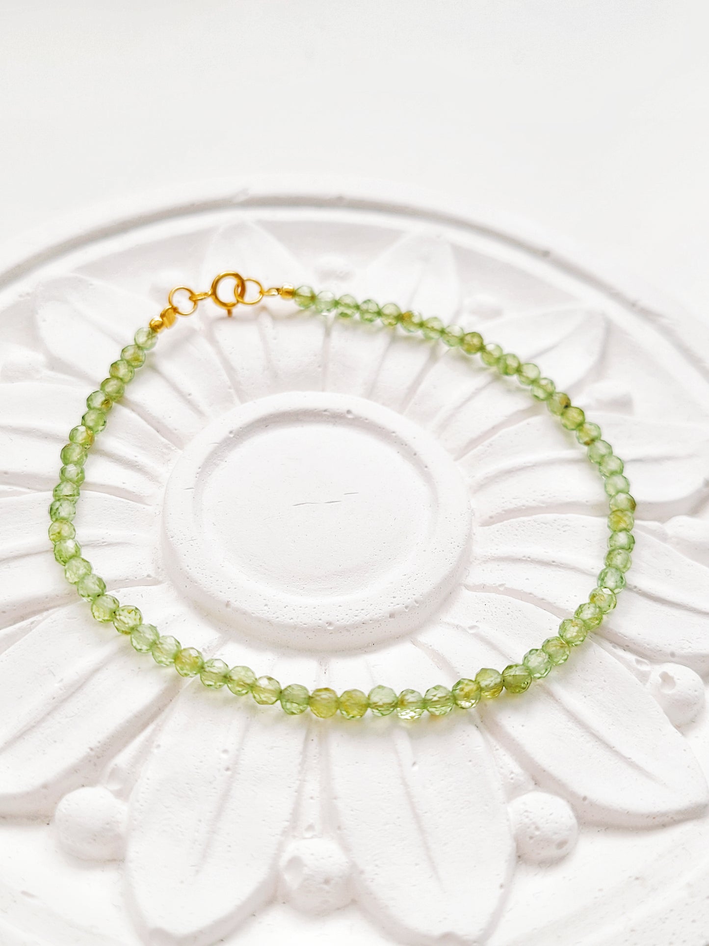 Peridot bracelet with gold clasp resting on flower plate