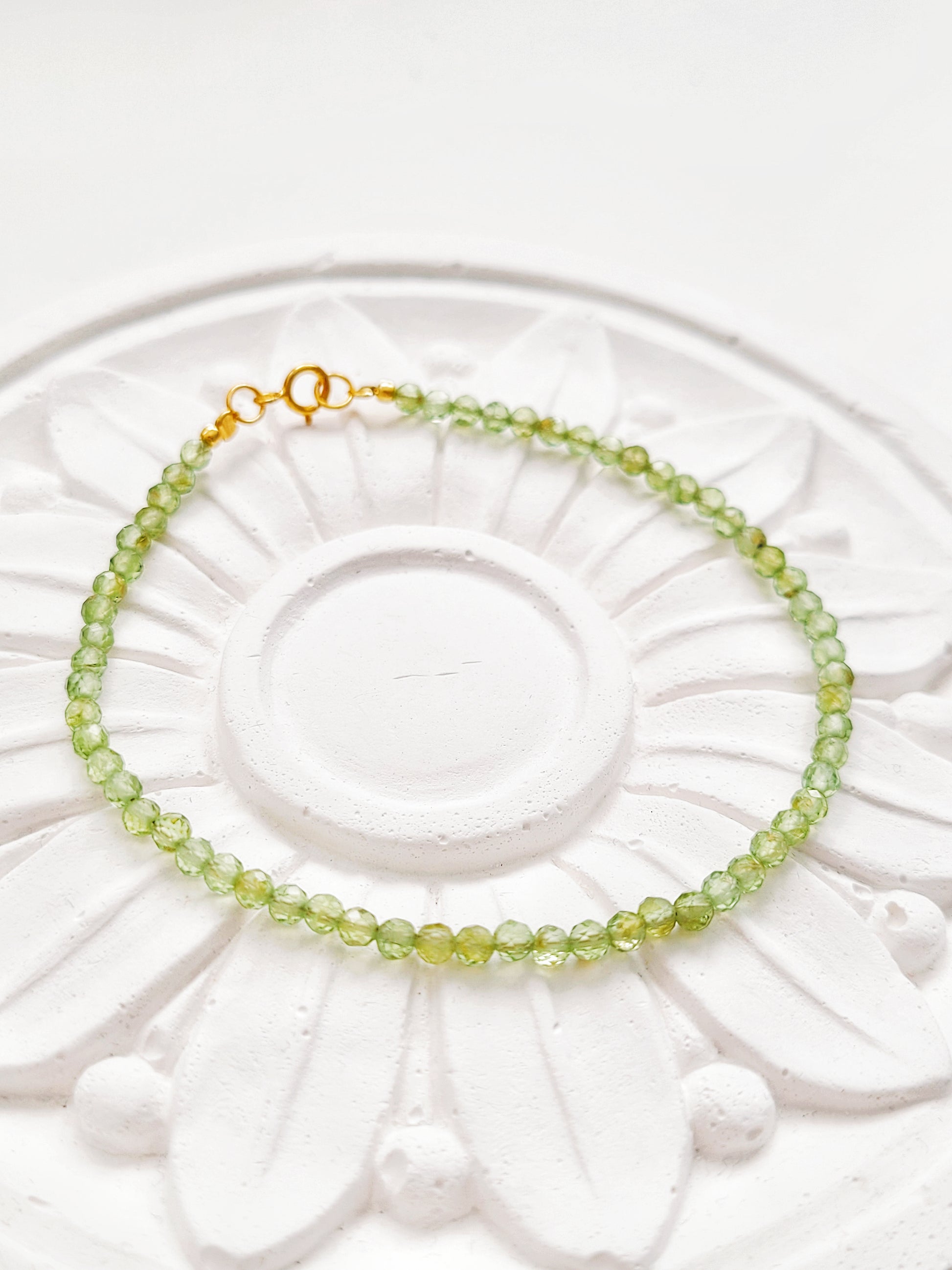 Peridot bracelet with gold clasp resting on flower plate