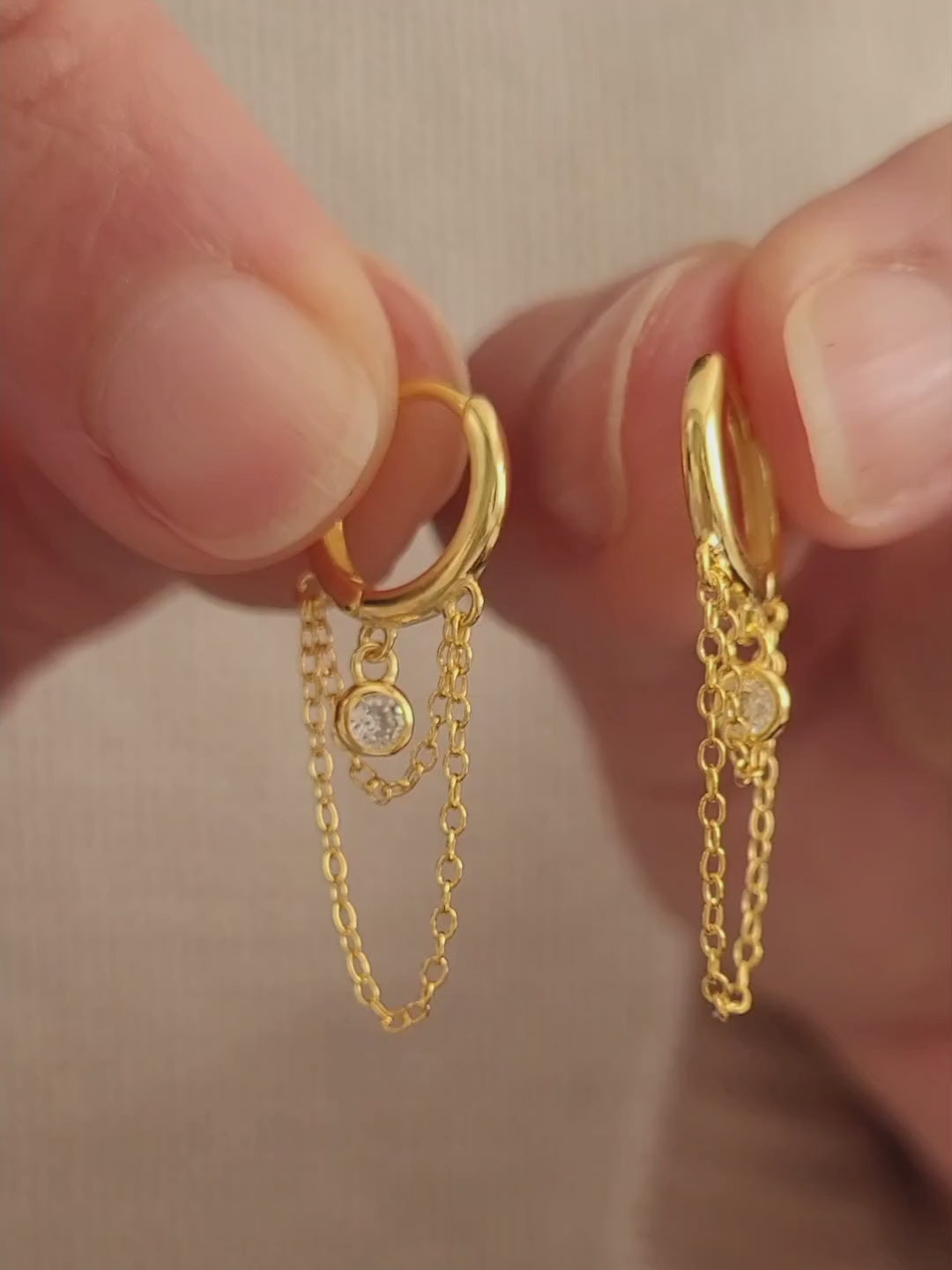 Close-up of a pair of gold double chain huggie earrings with a CZ diamond drop. Crafted in gold plated sterling silver, boho chic summer look.