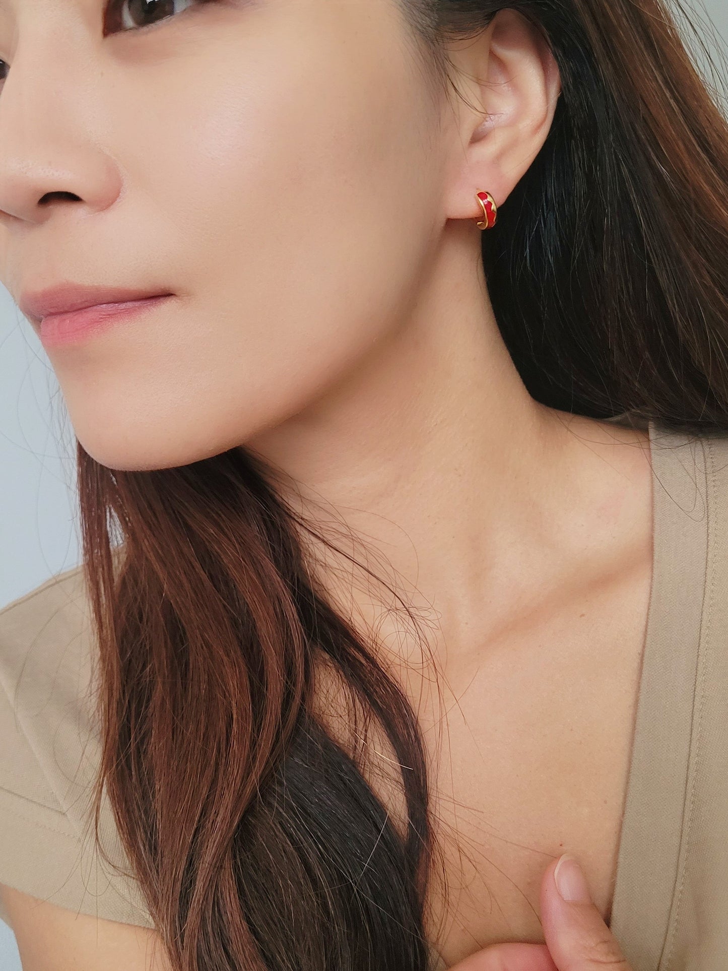 A woman showcasing her trendy red enamel hoop earrings.