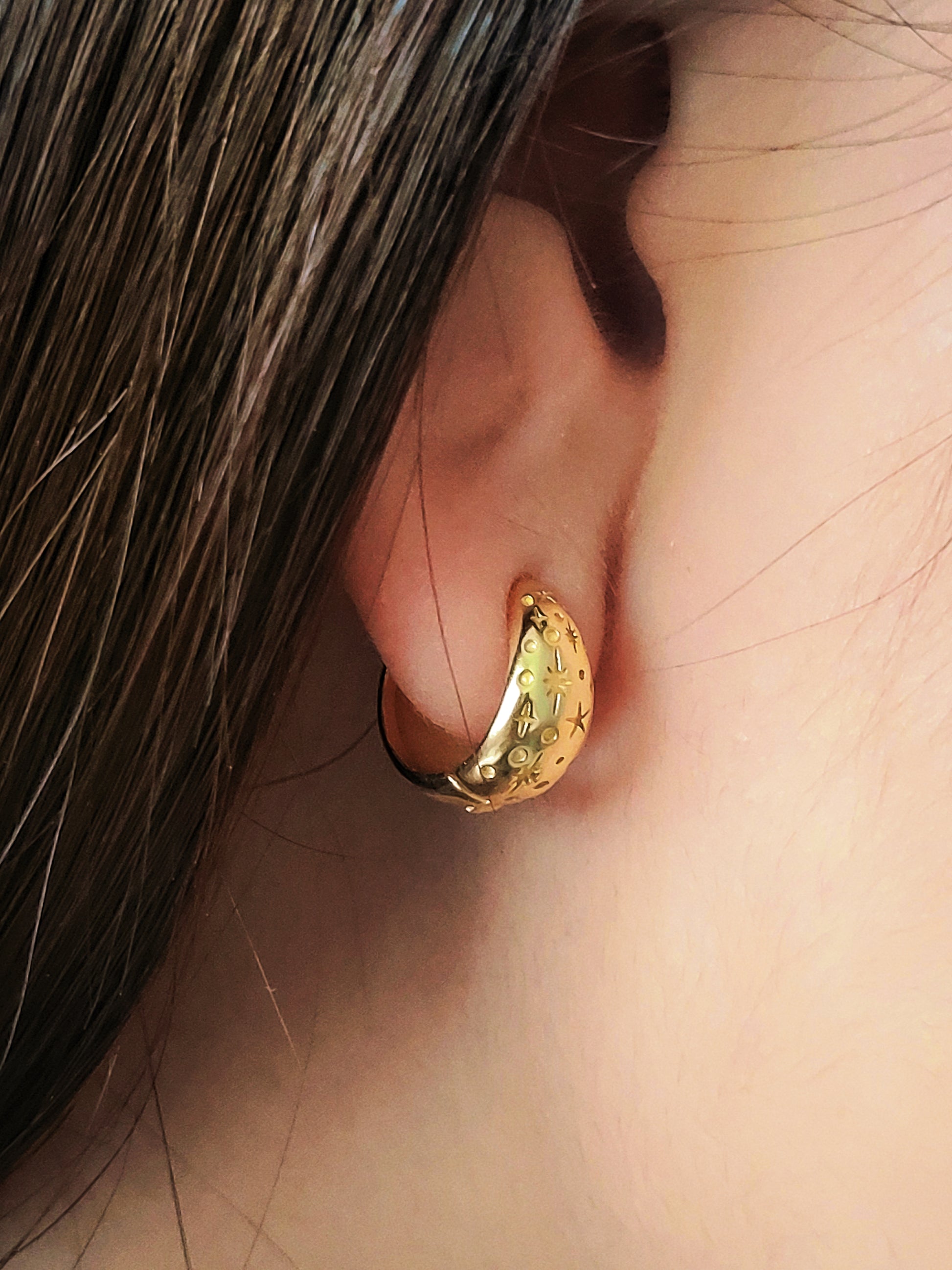Gold star huggie hoop earring worn on an ear with a close-up view