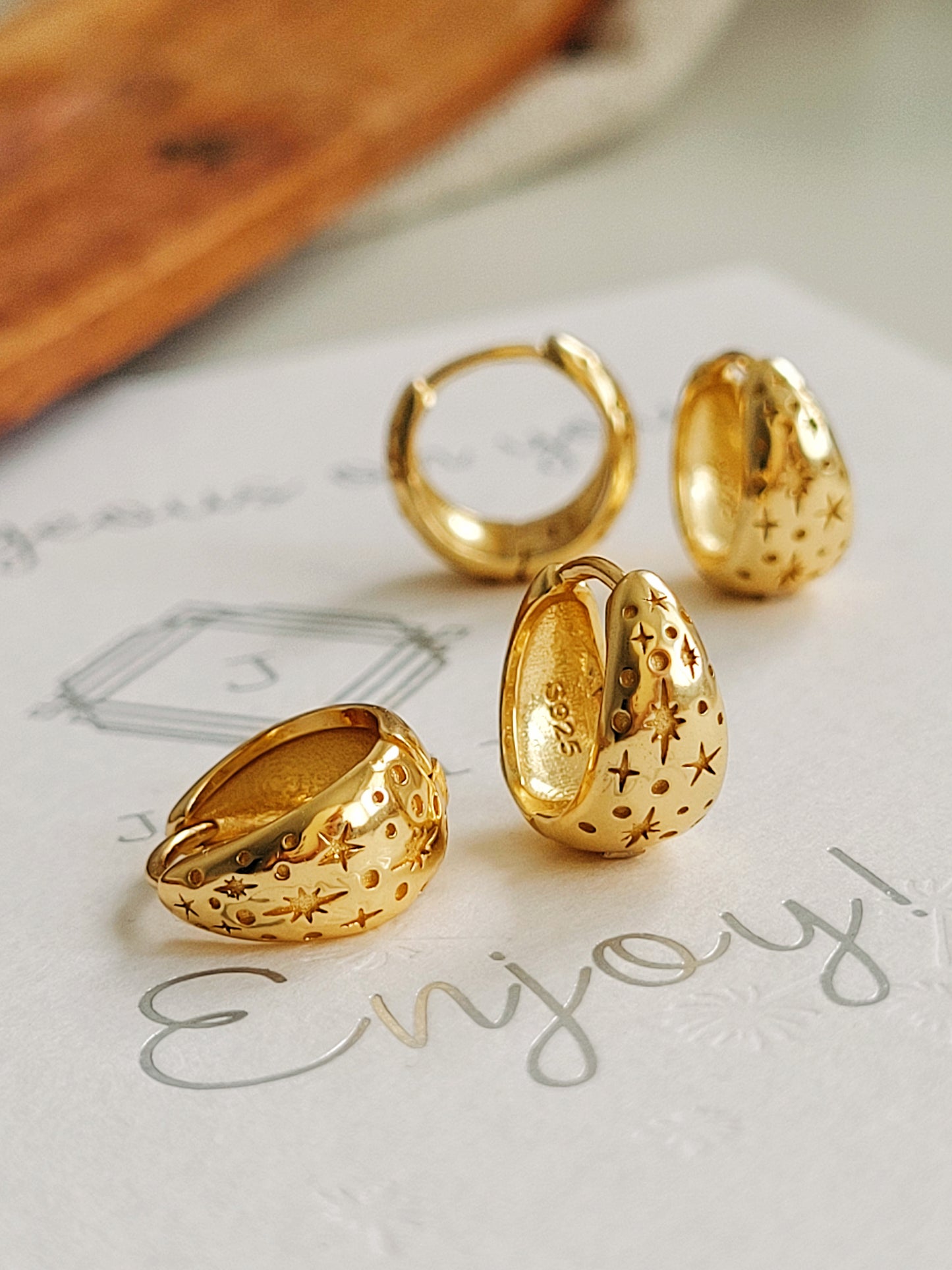 Gold Stars hoop earrings on a piece of paper with 'Enjoy' written on it