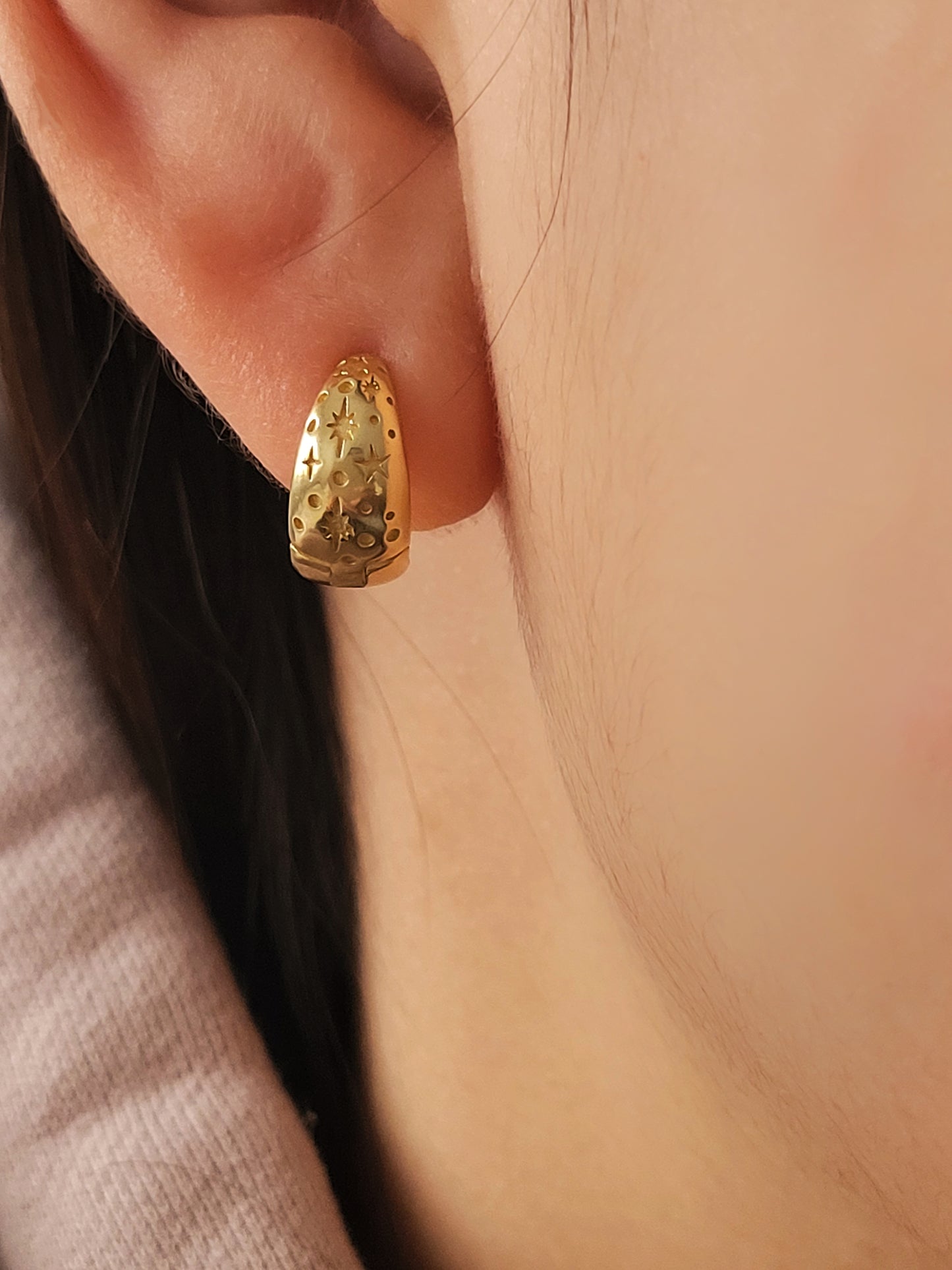 Gold earring featuring celestial star pattern worn on an ear with a neutral background
