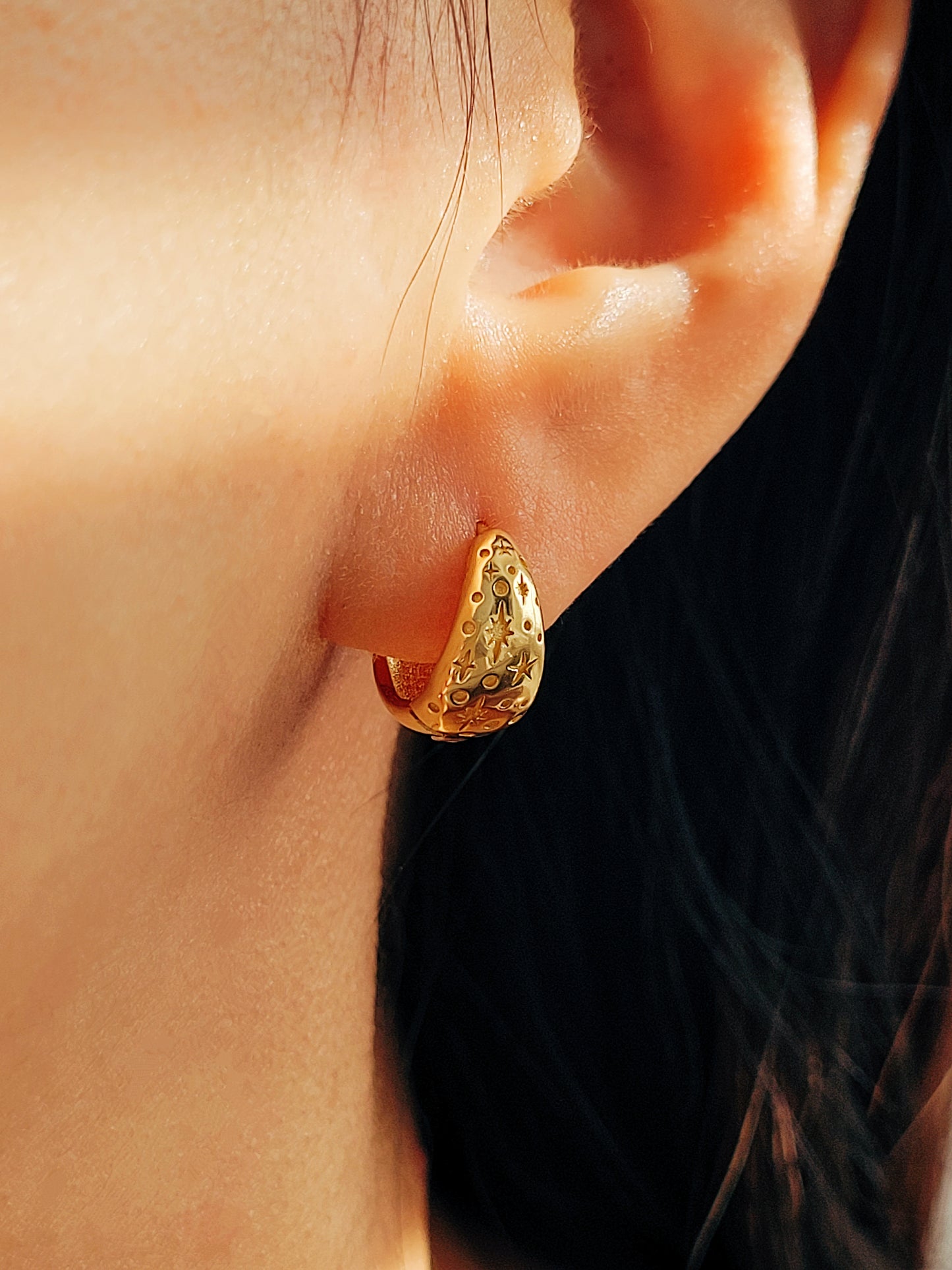 Close up of a starry huggie hoop earring worn on a woman's ear