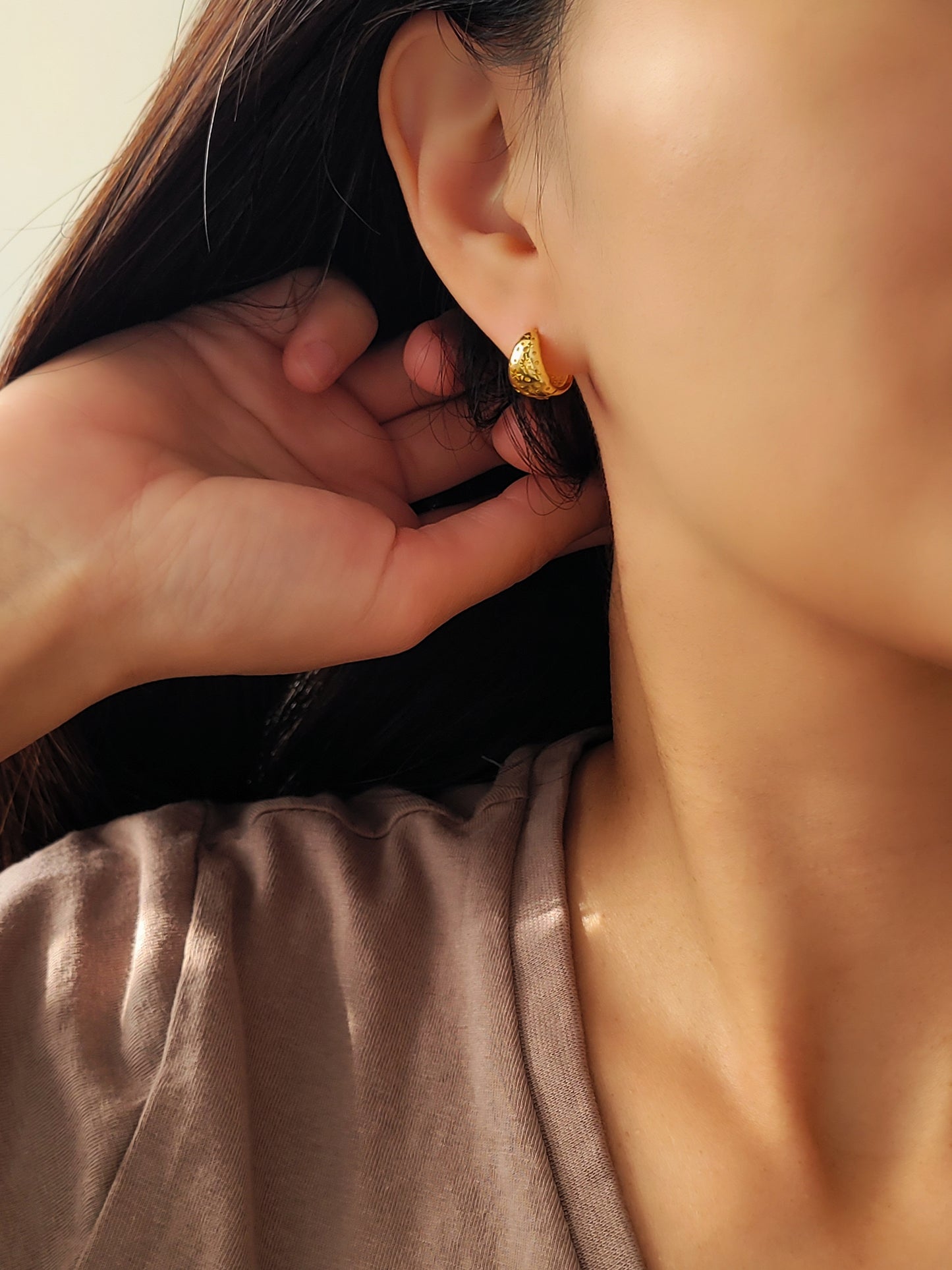 Close-up of a person wearing gold earrings with a neutral background
