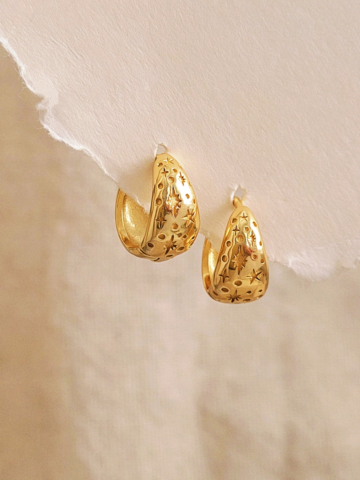 Gold hoop star earrings on a textured beige background