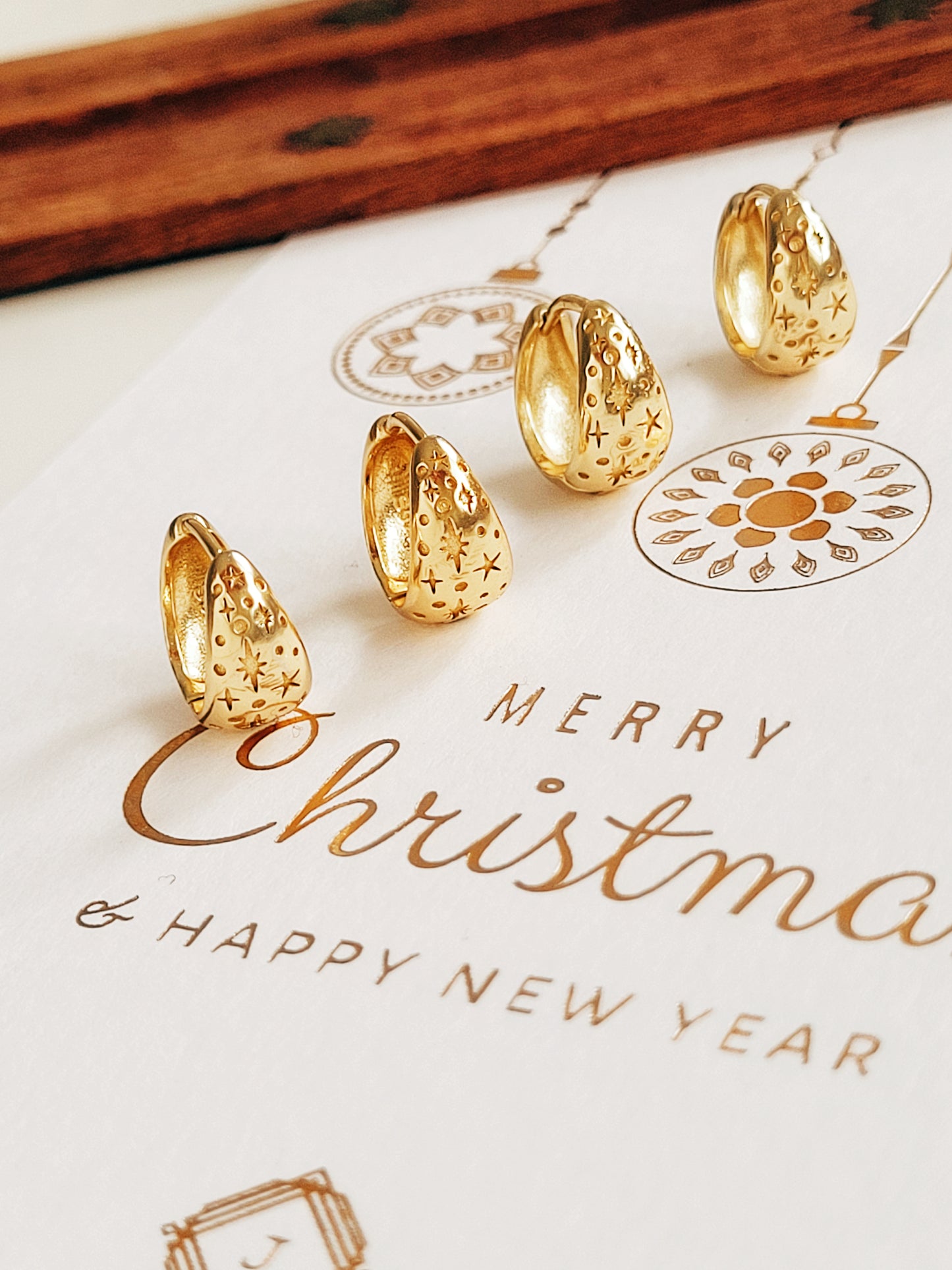 Gold star huggie earrings on a Christmas card with 'Merry Christmas & Happy New Year' text