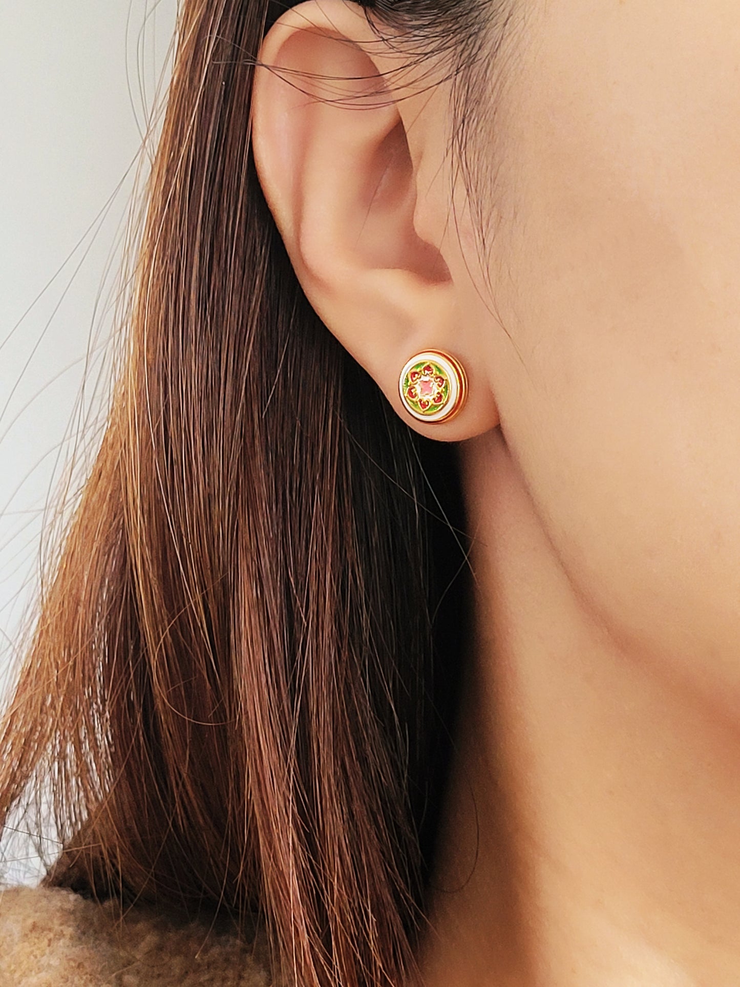 Close-up of a woman wearing a small, vintage-inspired gold stud earring with a floral ceramic tile design in pink, green, and red, styled in Victorian Gothic fashion. The earring sits elegantly on her earlobe, adding a touch of classic sophistication.