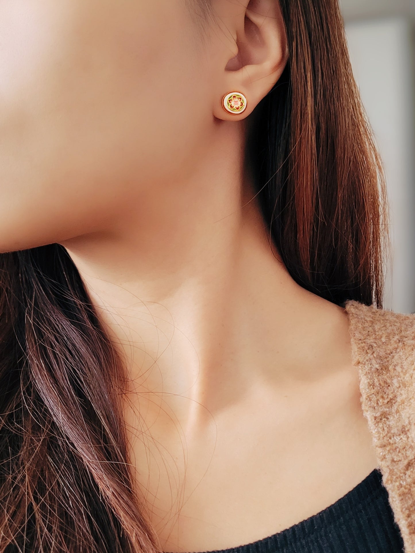 Close-up of a woman wearing a small, vintage-inspired gold stud earring with a floral ceramic tile design in pink, green, and red, styled in Victorian Gothic fashion. The earring sits elegantly on her earlobe, adding a touch of classic sophistication