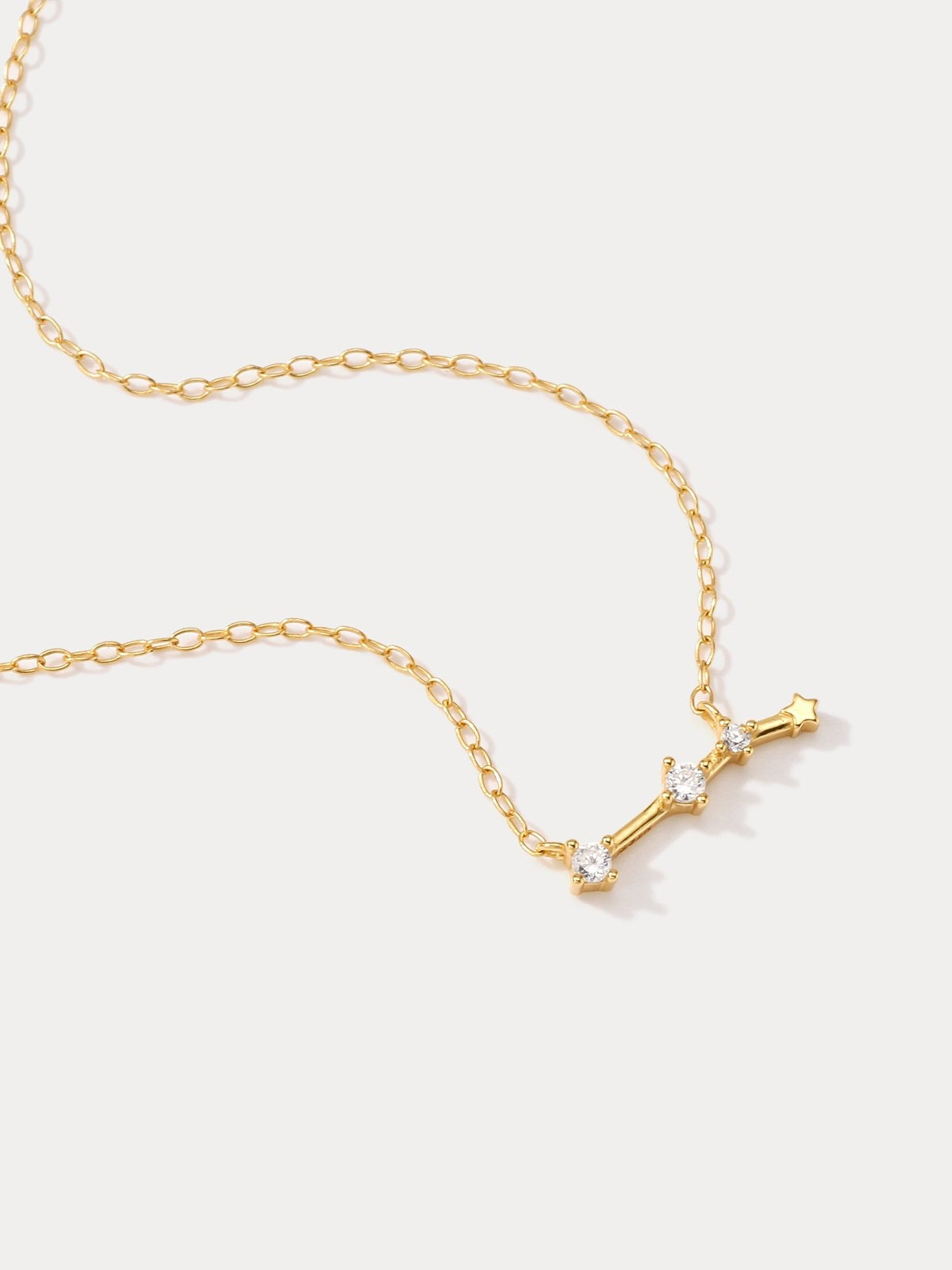 A dainty gold necklace with a pendant featuring a stylized Aries zodiac constellation sign with sparkling zircons.