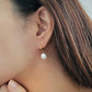 Side profile of a person wearing a dainty gold and pearl earring, emphasizing the natural luster of the pearl.