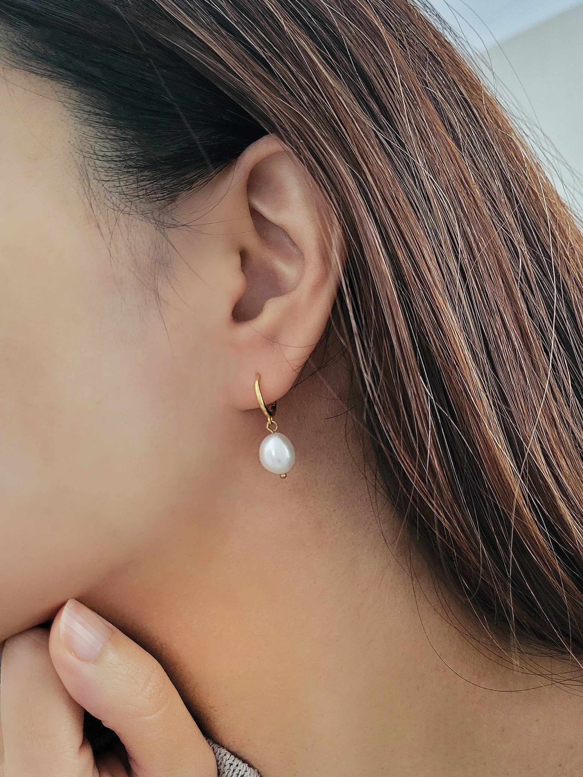 Side profile of a person wearing a dainty gold and pearl earring, emphasizing the natural luster of the pearl.