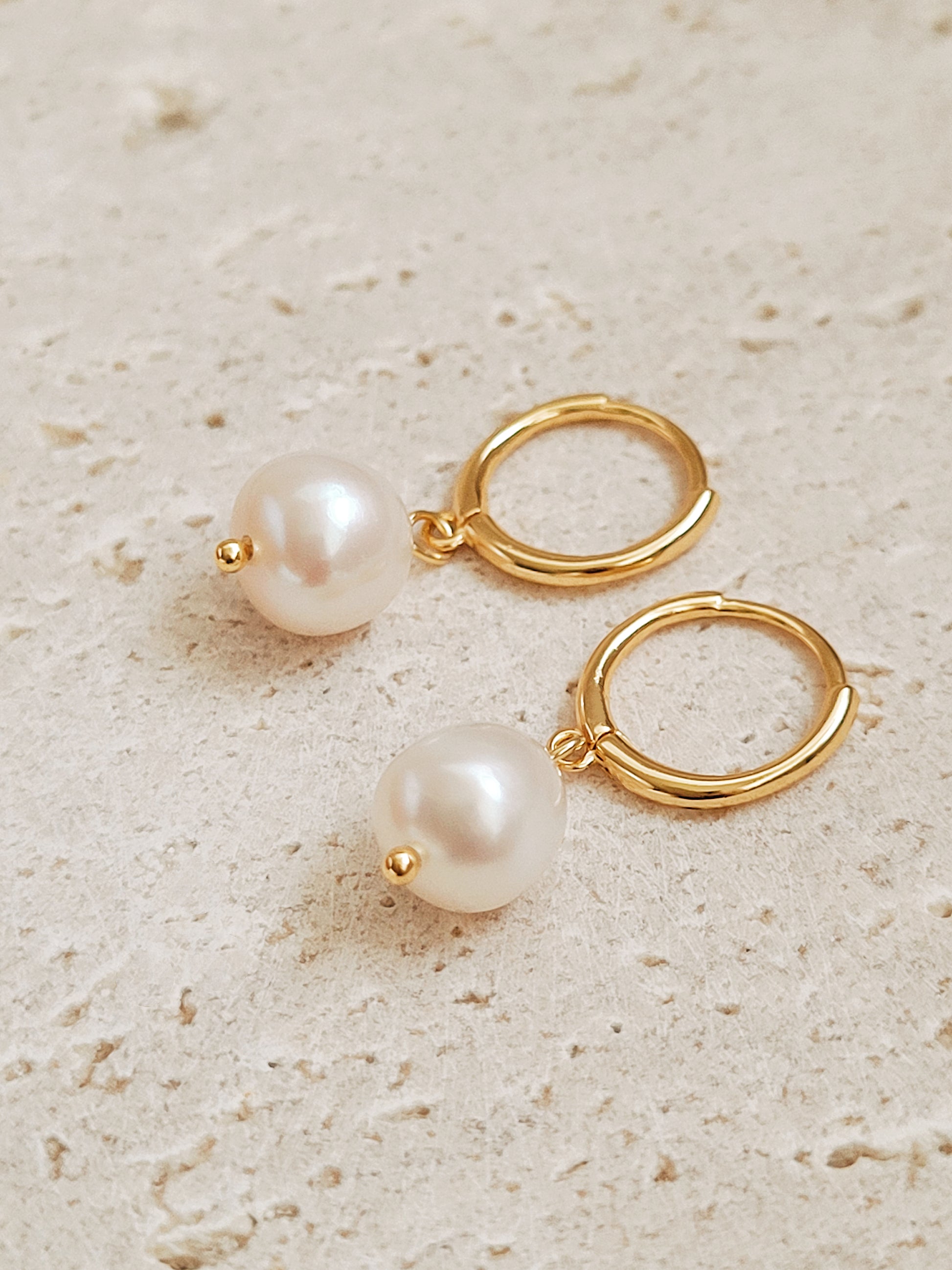 Close-up of gold hoop earrings with dangling pearls, highlighting their polished and timeless craftsmanship.