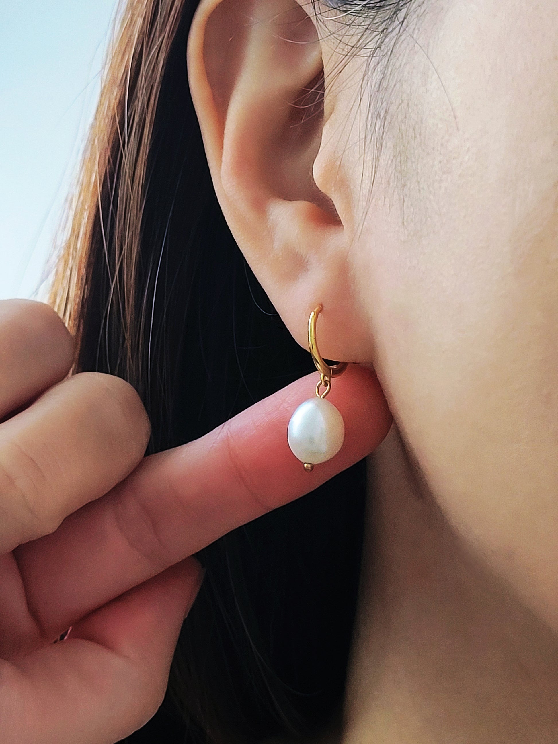 Close-up of a woman wearing a gold-plated pearl drop earring, showcasing its elegant and minimalist design.