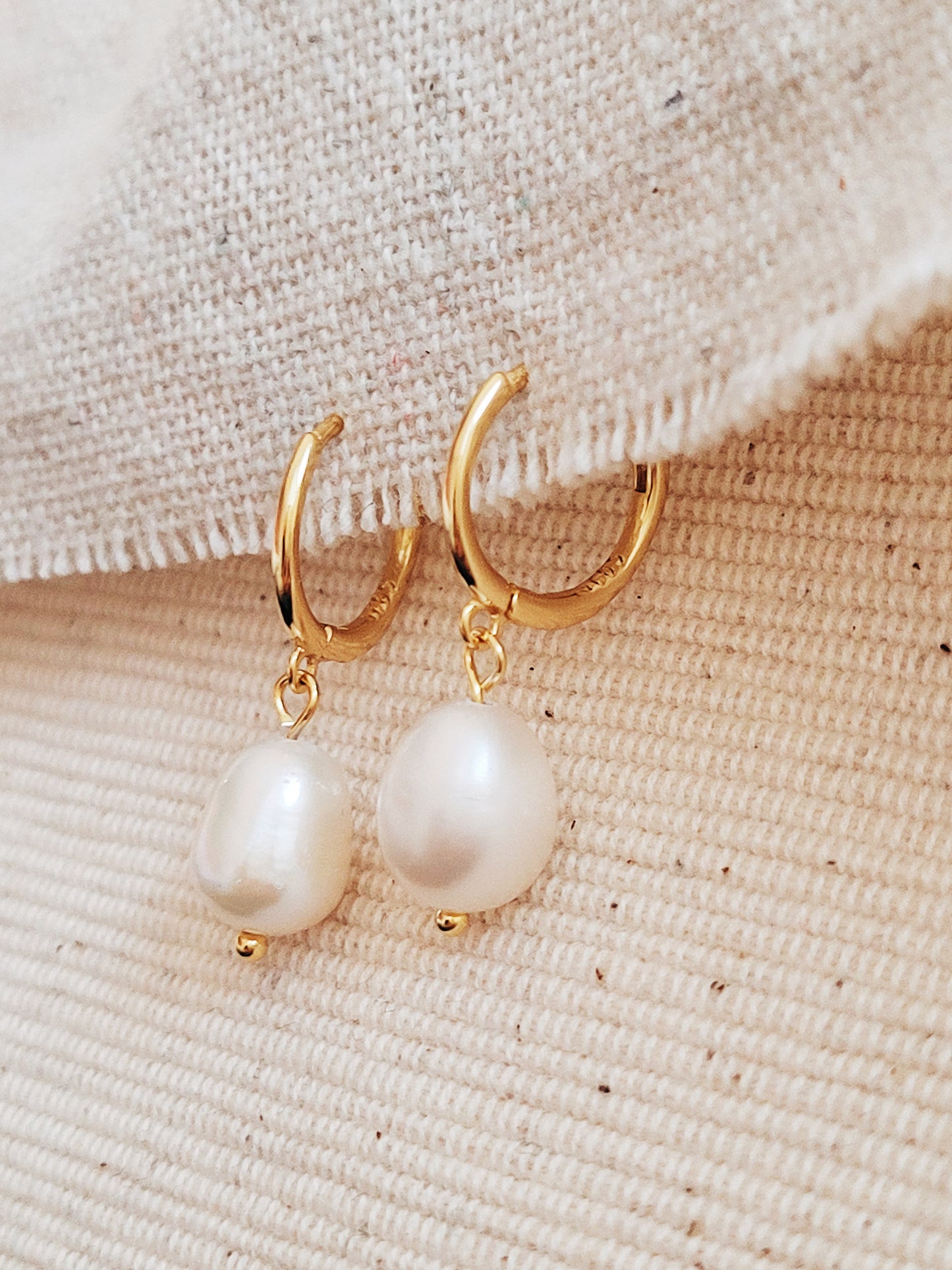 Minimalist gold and pearl drop earrings displayed against a soft beige backdrop for a refined look.