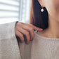 Gold huggie hoop earring with a dangling freshwater pearl, worn for a sophisticated and timeless look.
