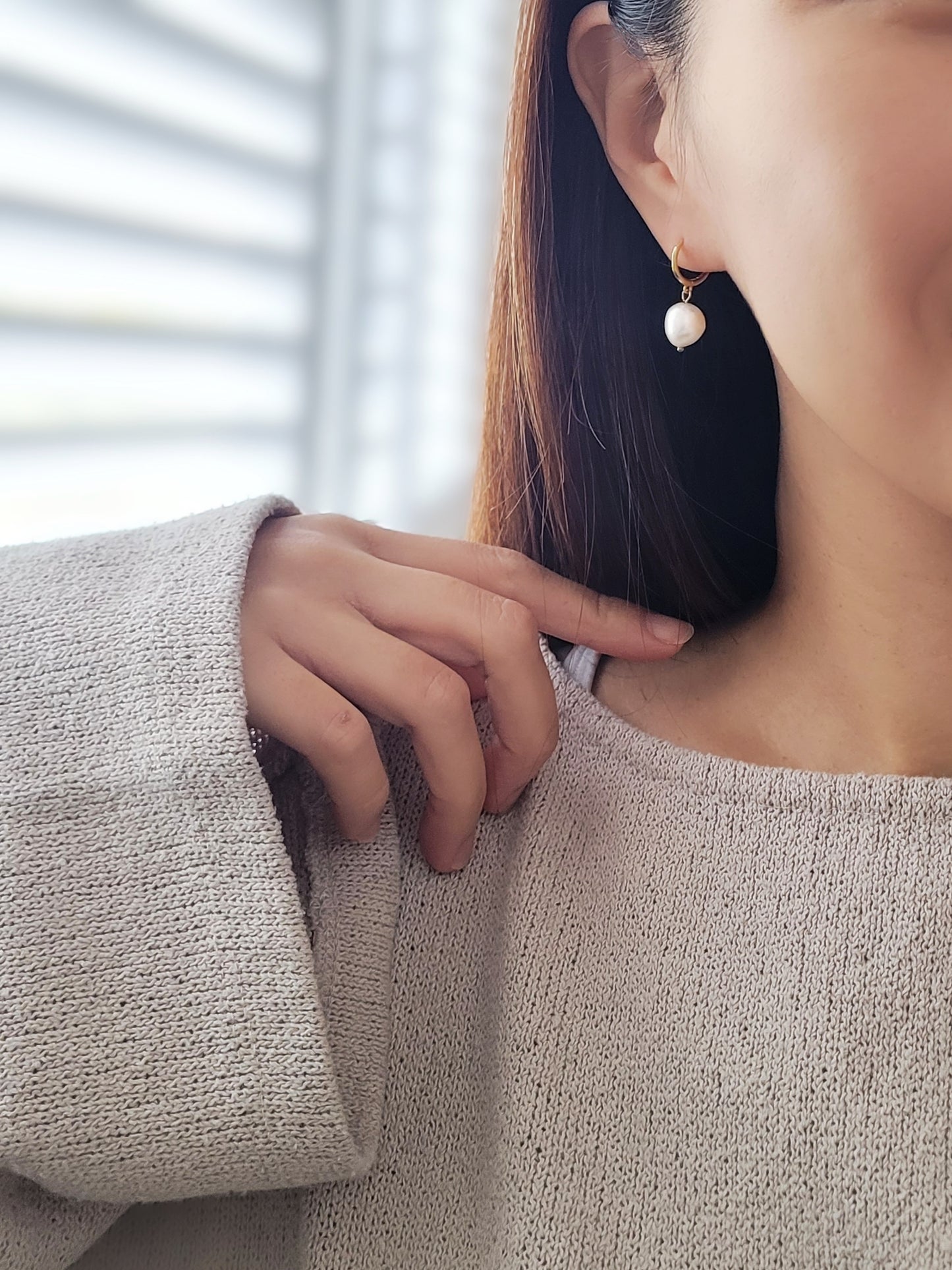 Gold huggie hoop earring with a dangling freshwater pearl, worn for a sophisticated and timeless look.