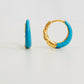 Close-up of bright blue enamel twisted hoop earrings on a white surface.