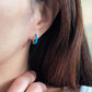 Close-up of bright blue enamel twisted hoop earrings on a white surface.