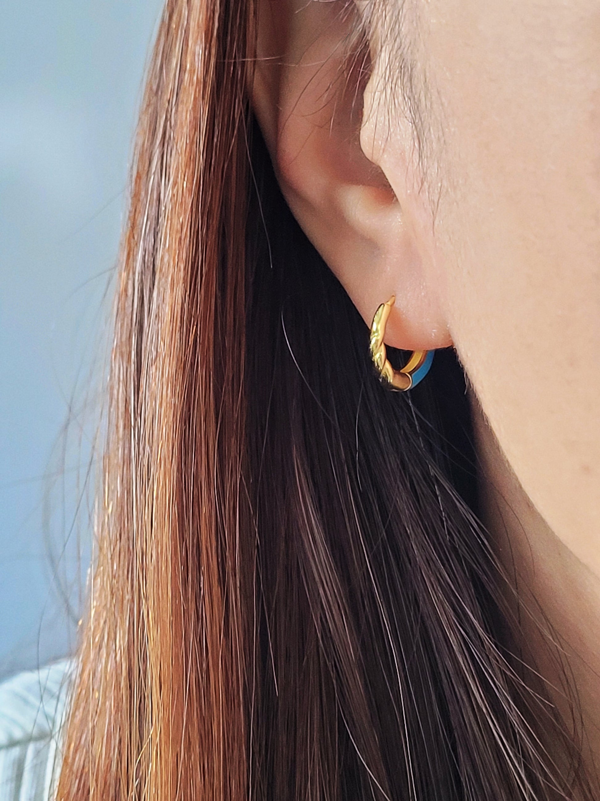 Close-up of bright blue enamel twisted hoop earrings on a white surface.