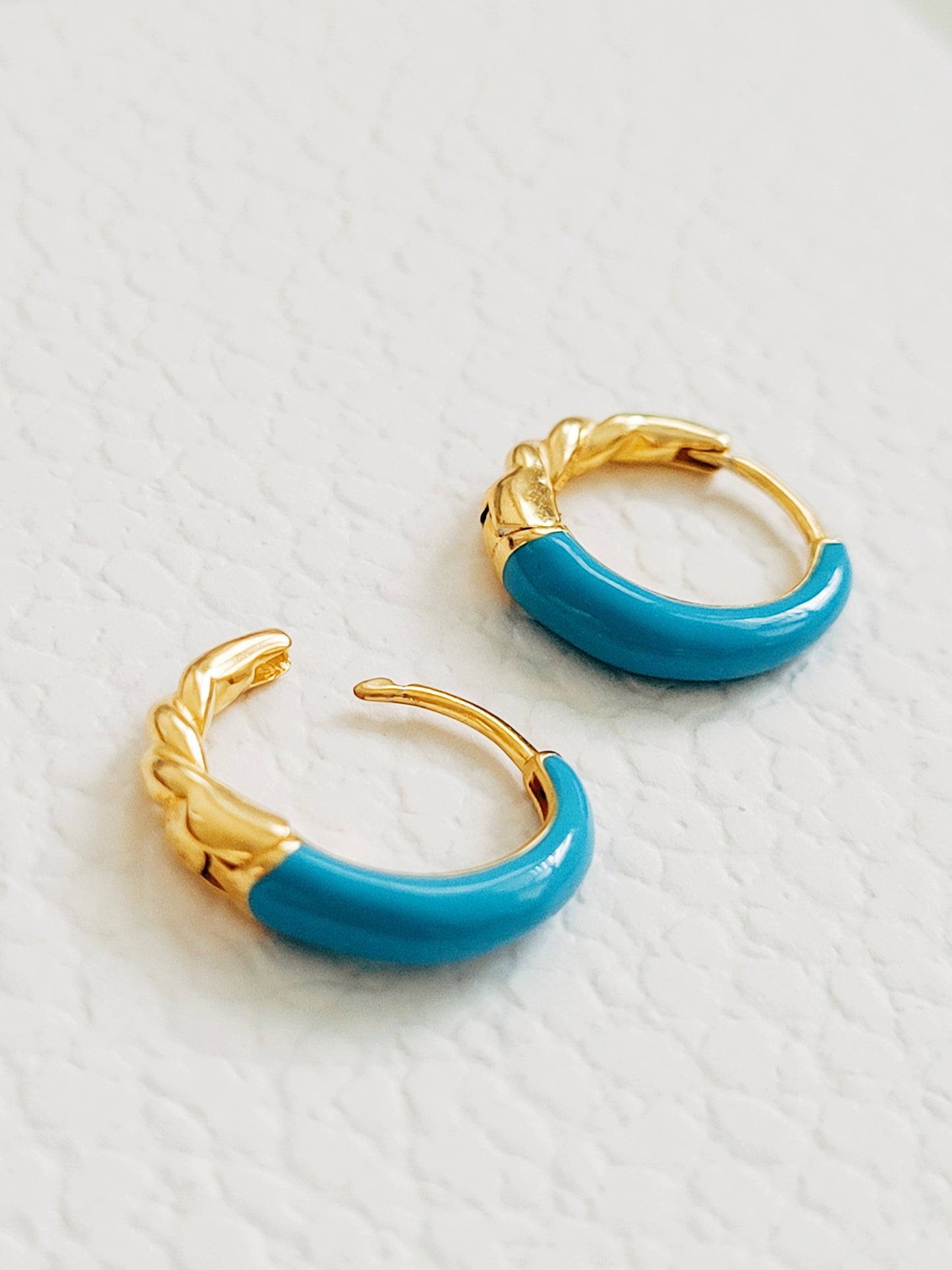 Close-up of bright blue enamel twisted hoop earrings on a white surface.