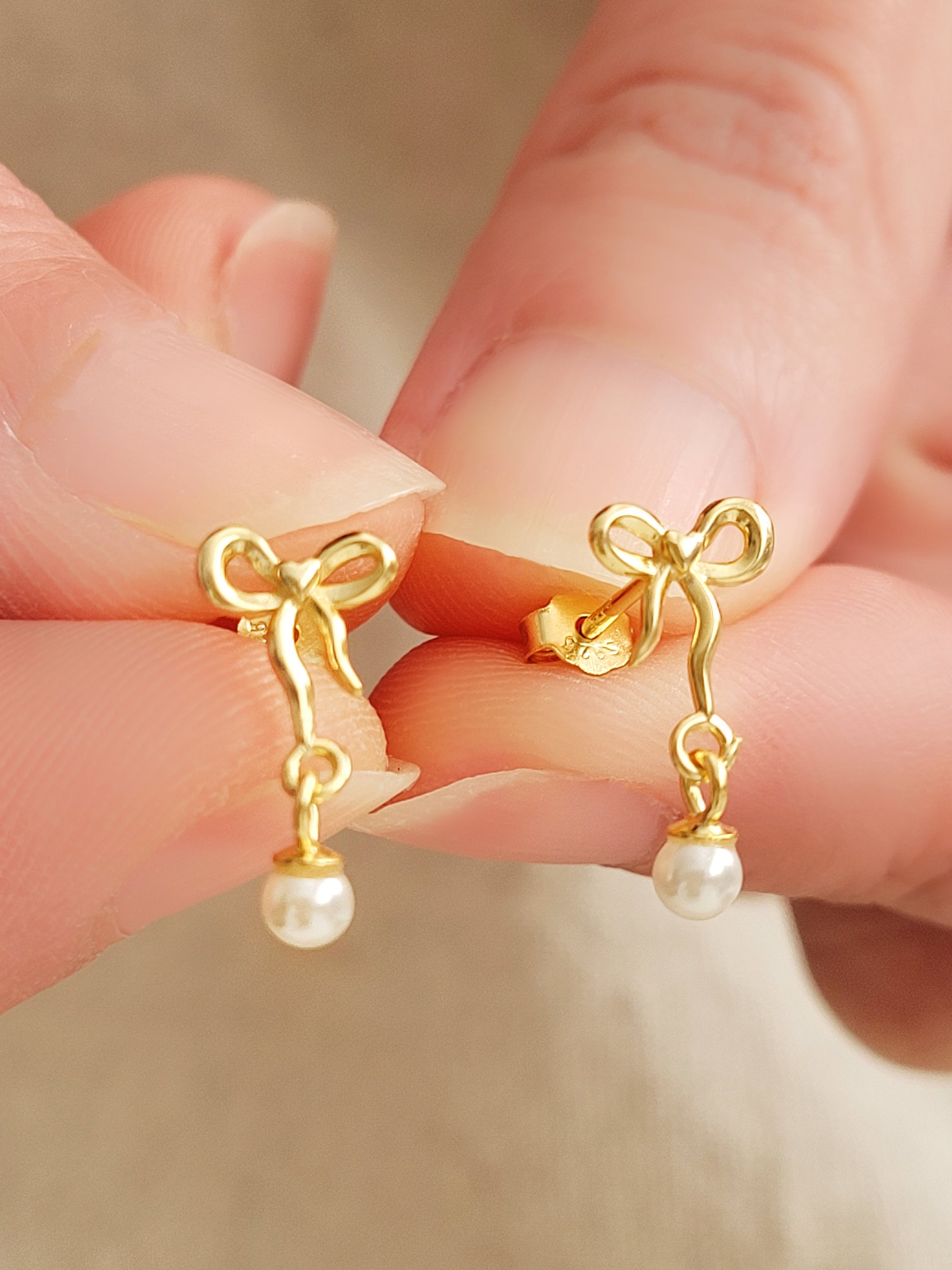 Close-up view of gold bow stud earrings with freshwater pearl dangle, showing intricate bow design. Crafted in gold plated 925 sterling silver. Perfect bridal jewellery.