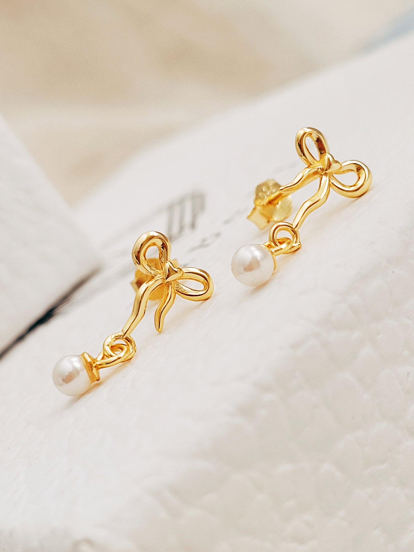 Close-up view of gold bow stud earrings with freshwater pearl dangle, showing intricate bow design. Crafted in gold plated 925 sterling silver. Perfect jewellery gift for her.