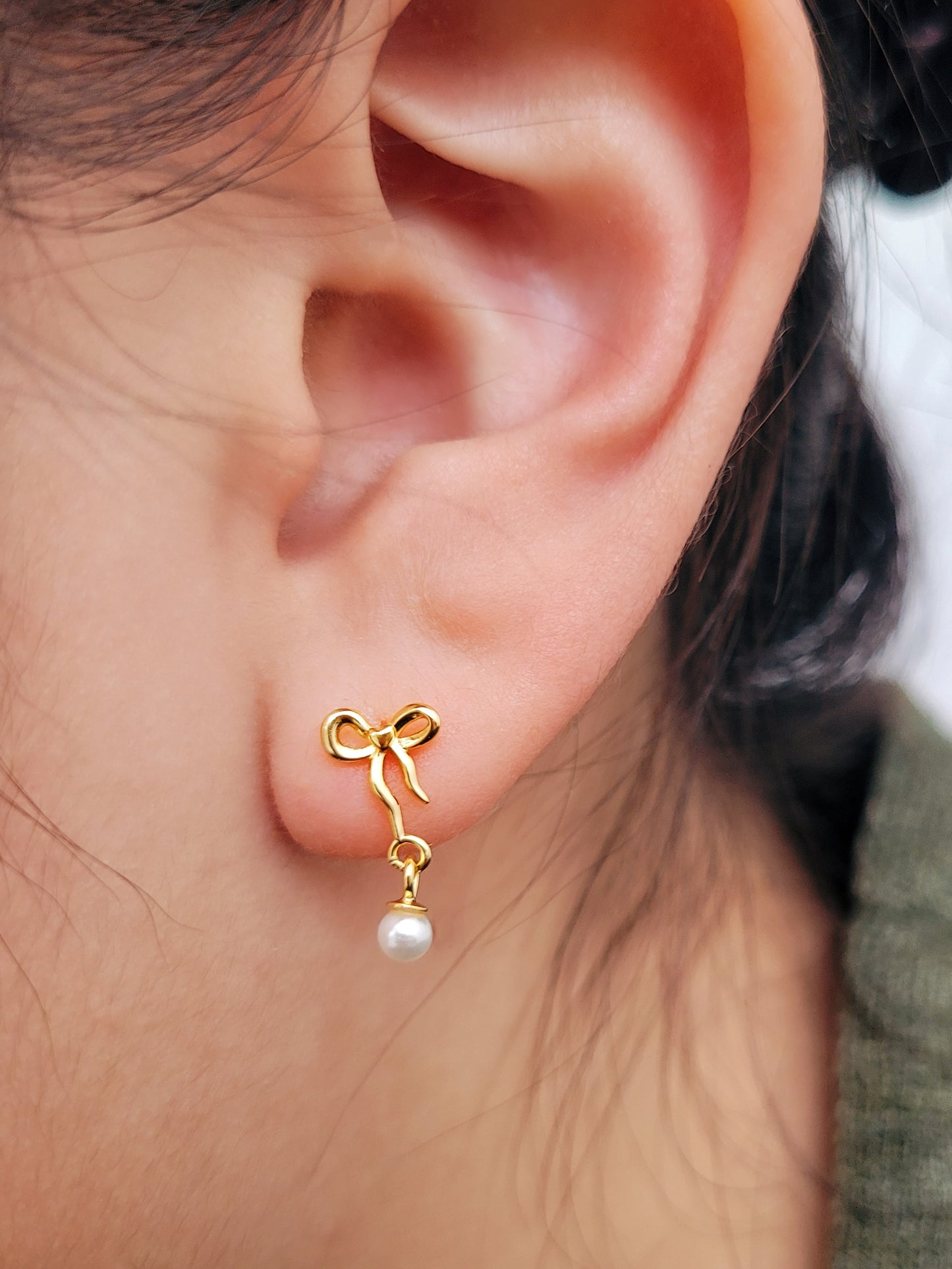 Close-up view of gold bow stud earrings with freshwater pearl dangle, showing intricate bow design. Crafted in gold plated 925 sterling silver. Perfect jewellery gift for her.