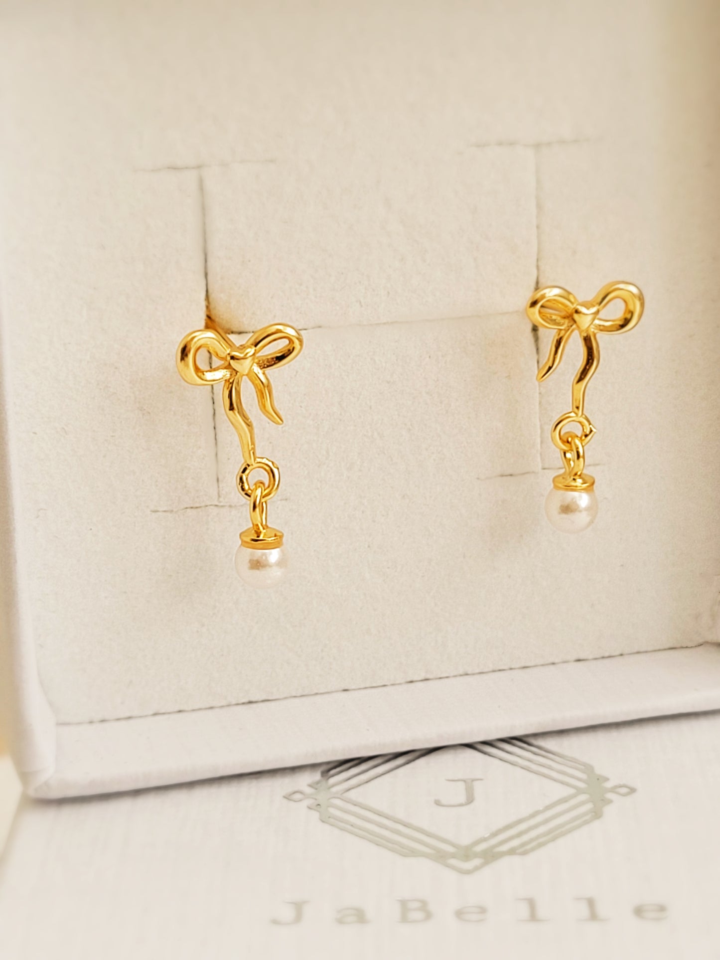 Close-up view of gold bow stud earrings with freshwater pearl dangle, showing intricate bow design. Crafted in gold plated 925 sterling silver. Perfect jewellery gift for her.