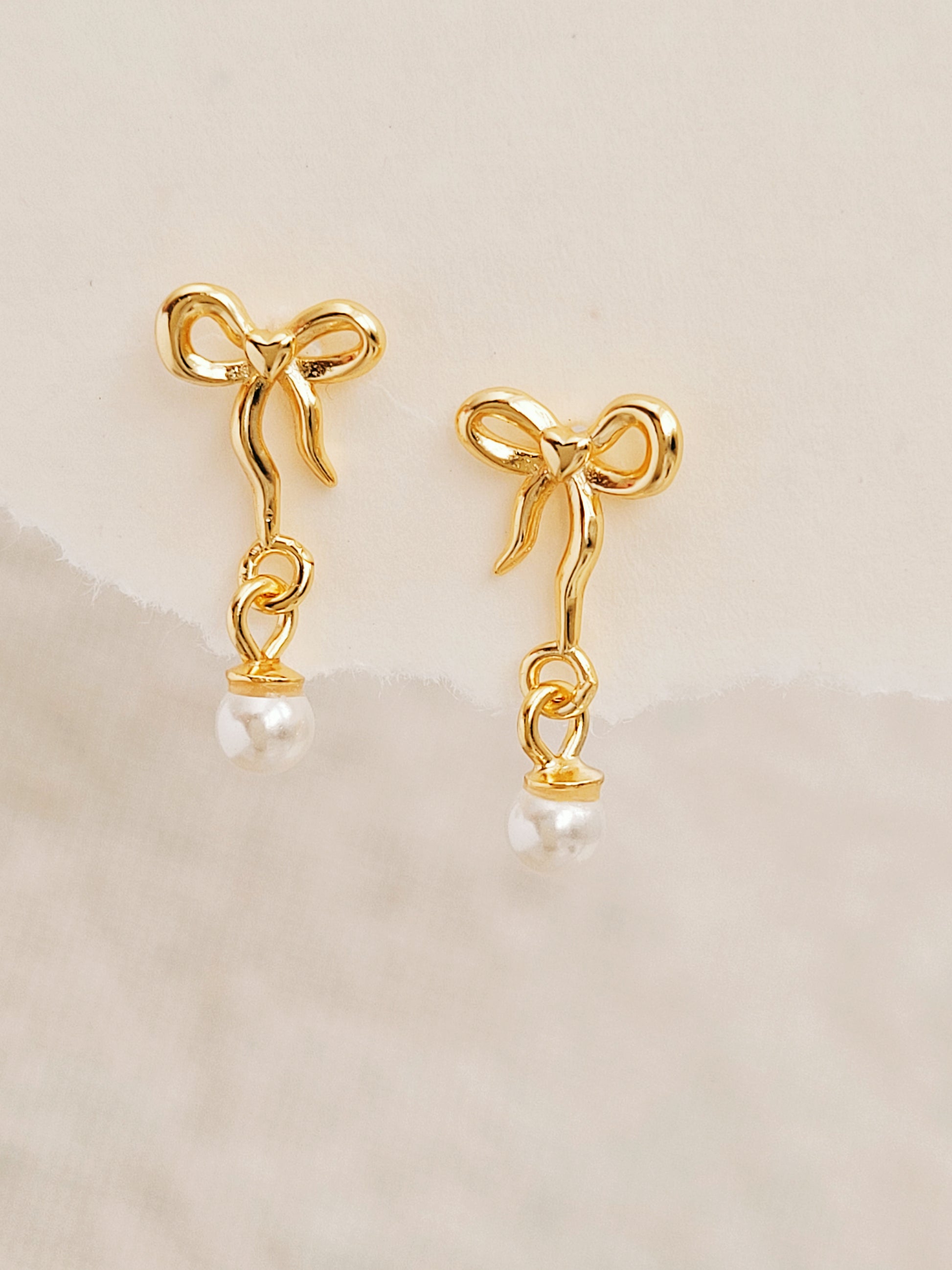 Close-up view of gold bow stud earrings with freshwater pearl dangle, showing intricate bow design. Crafted in gold plated 925 sterling silver. Perfect jewellery gift for her.