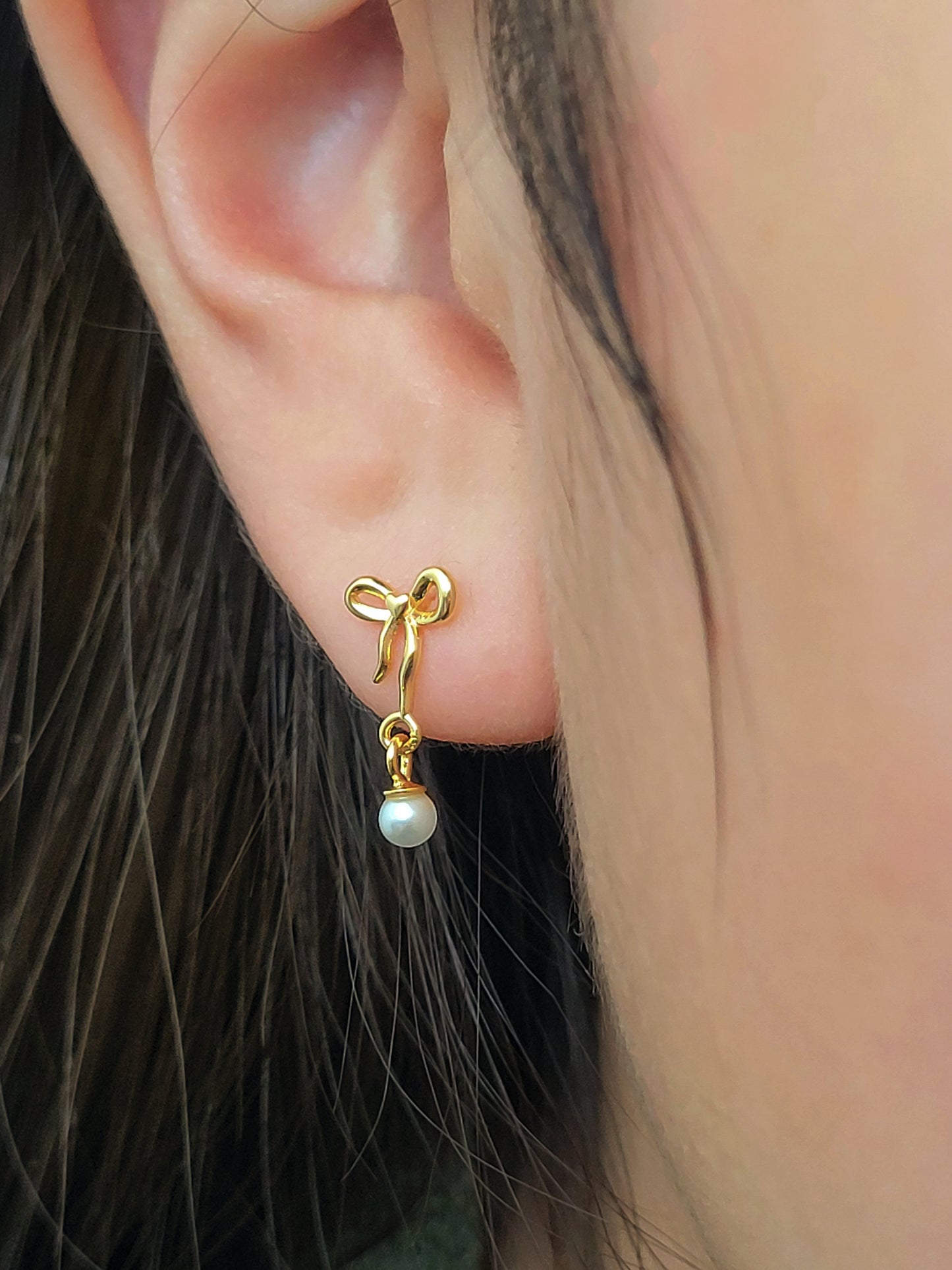 Close-up view of gold bow stud earrings with freshwater pearl dangle, showing intricate bow design. Crafted in gold plated 925 sterling silver. Perfect jewellery gift for her.