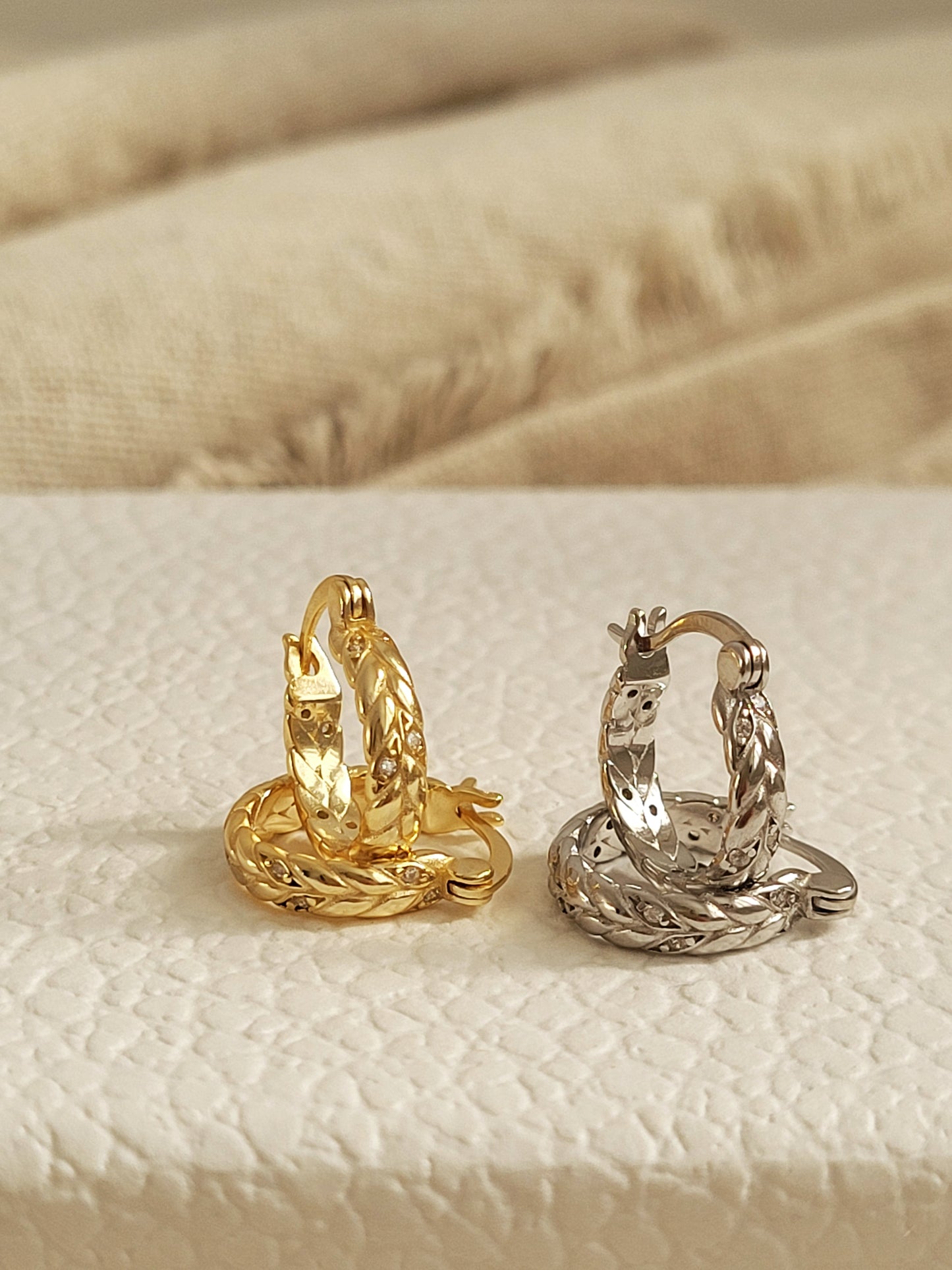 Dainty gold and silver huggie hoop earrings on a textured beige surface