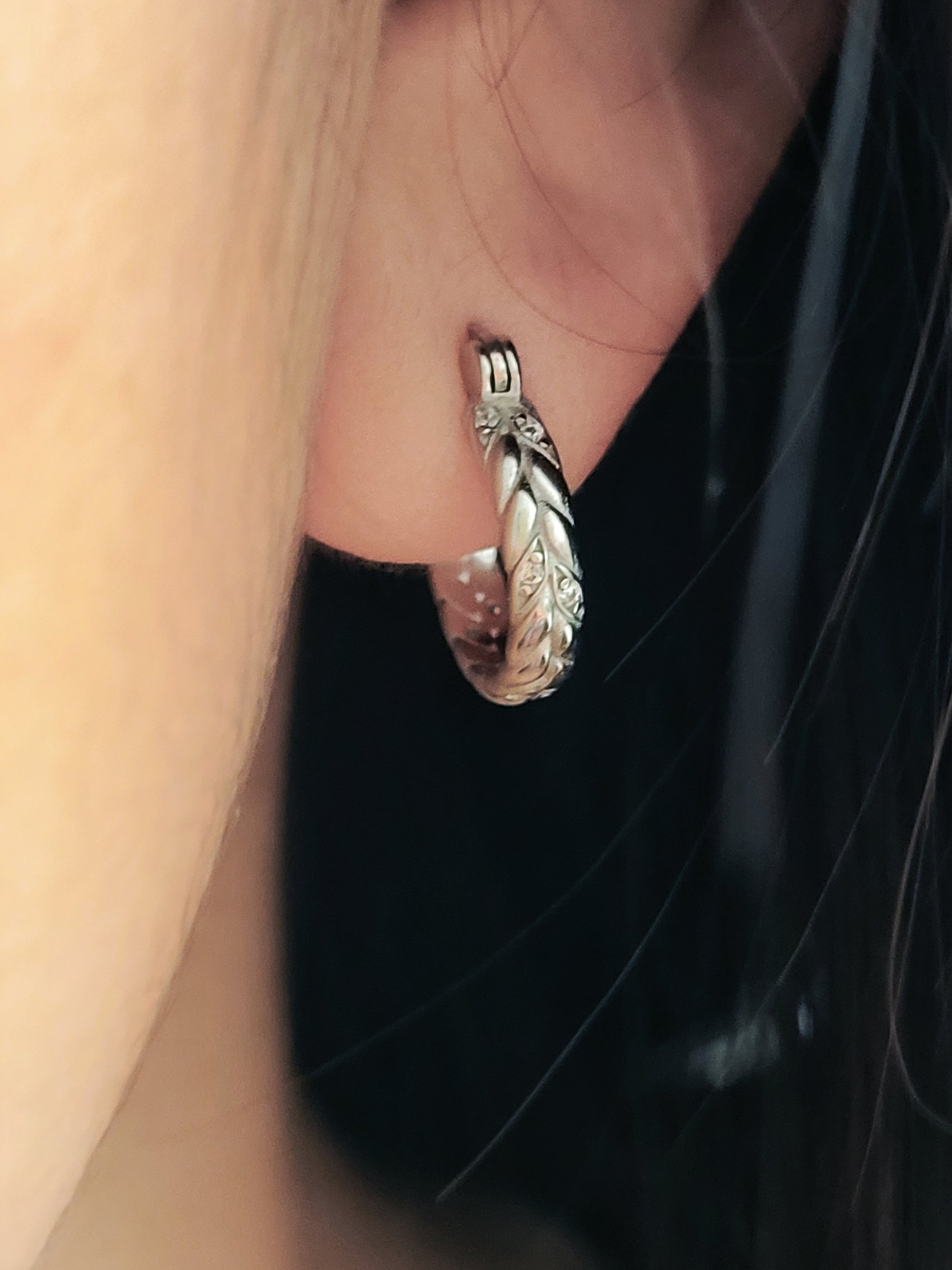 Silver hoop earring with braided texture worn by a woman