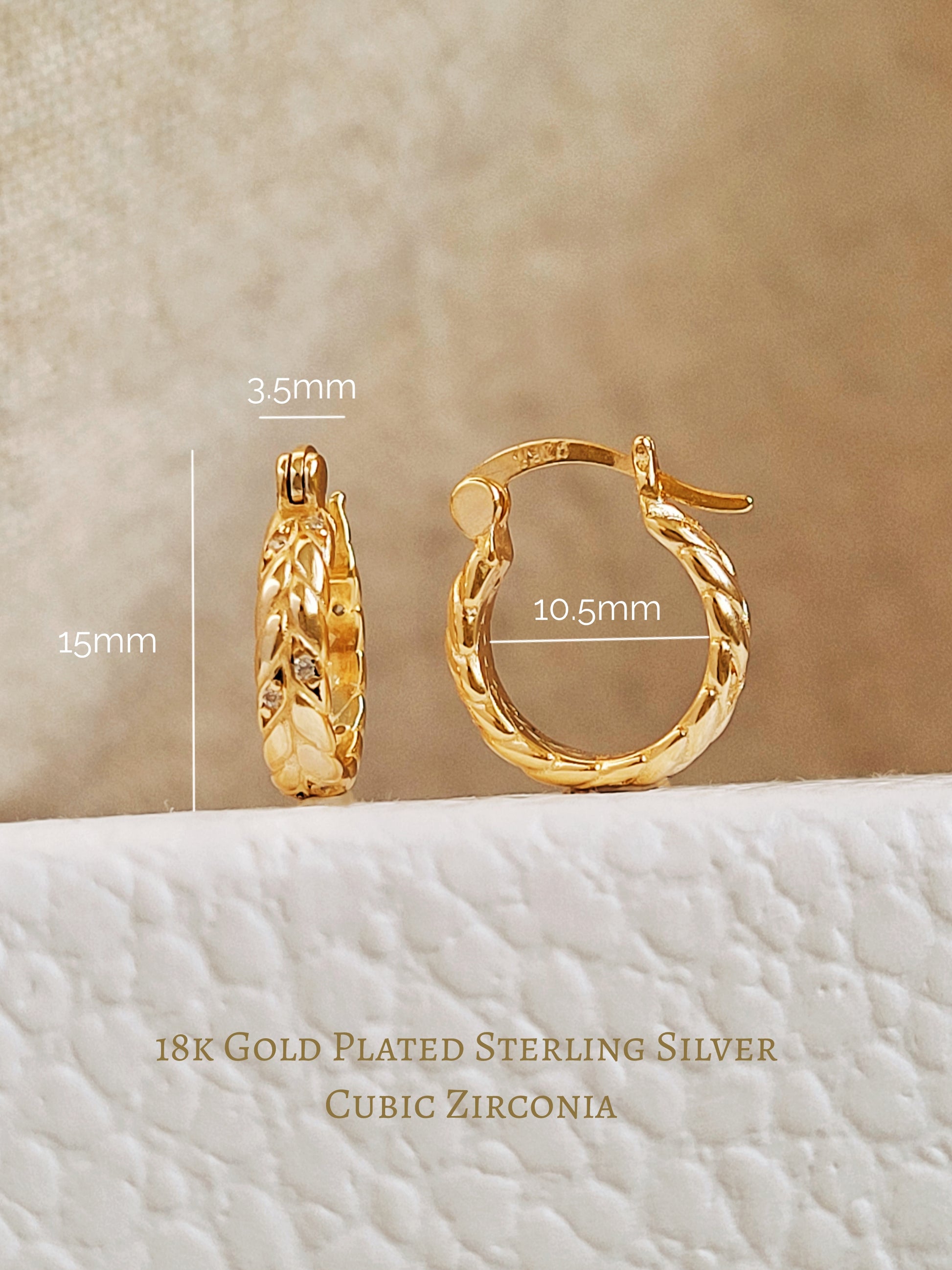 Gold hoop earrings with measurements on a textured beige background