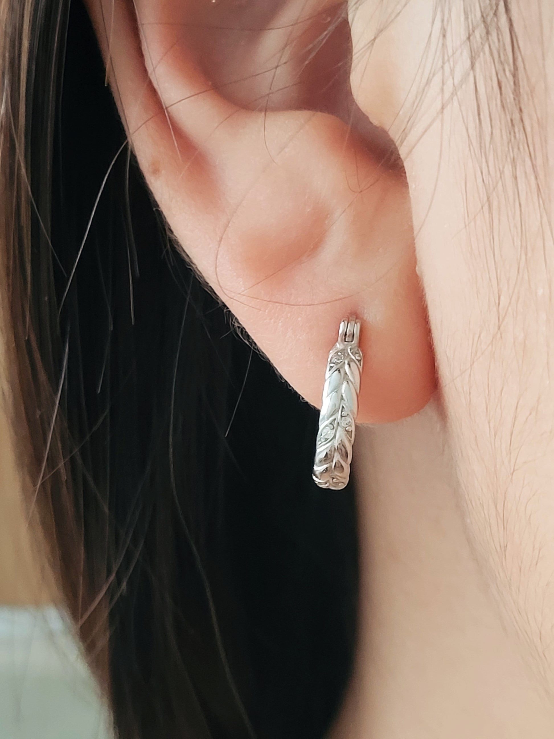 Dainty silver hoop earring with braided details worn by a woman.
