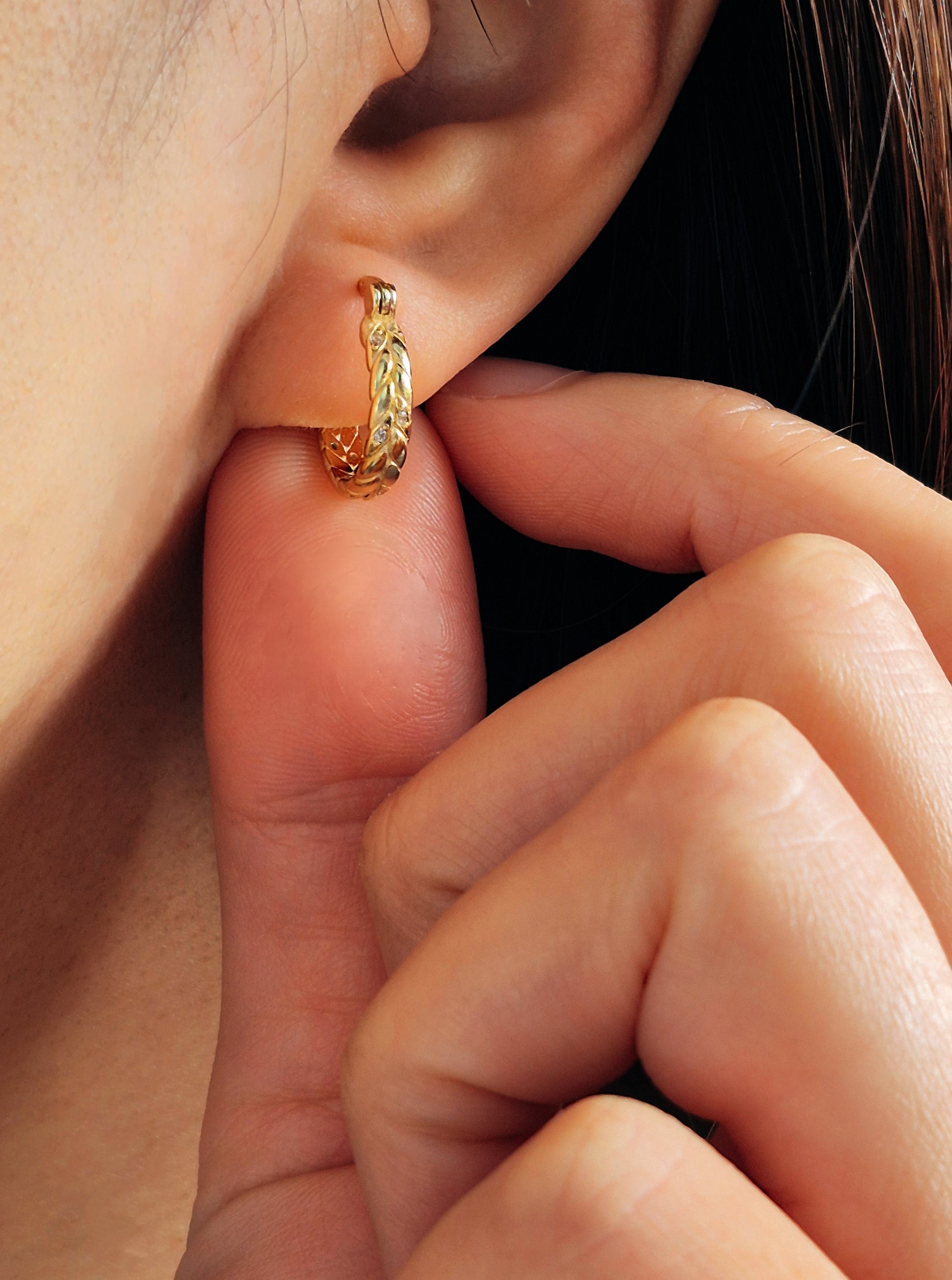Dainty gold hoop earring with braided details worn by a woman.