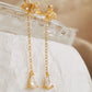 A pair of dainty gold butterfly earrings with chain drops on a white fabric background.