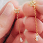Gold butterfly and teardrop earrings held between fingers against a neutral background