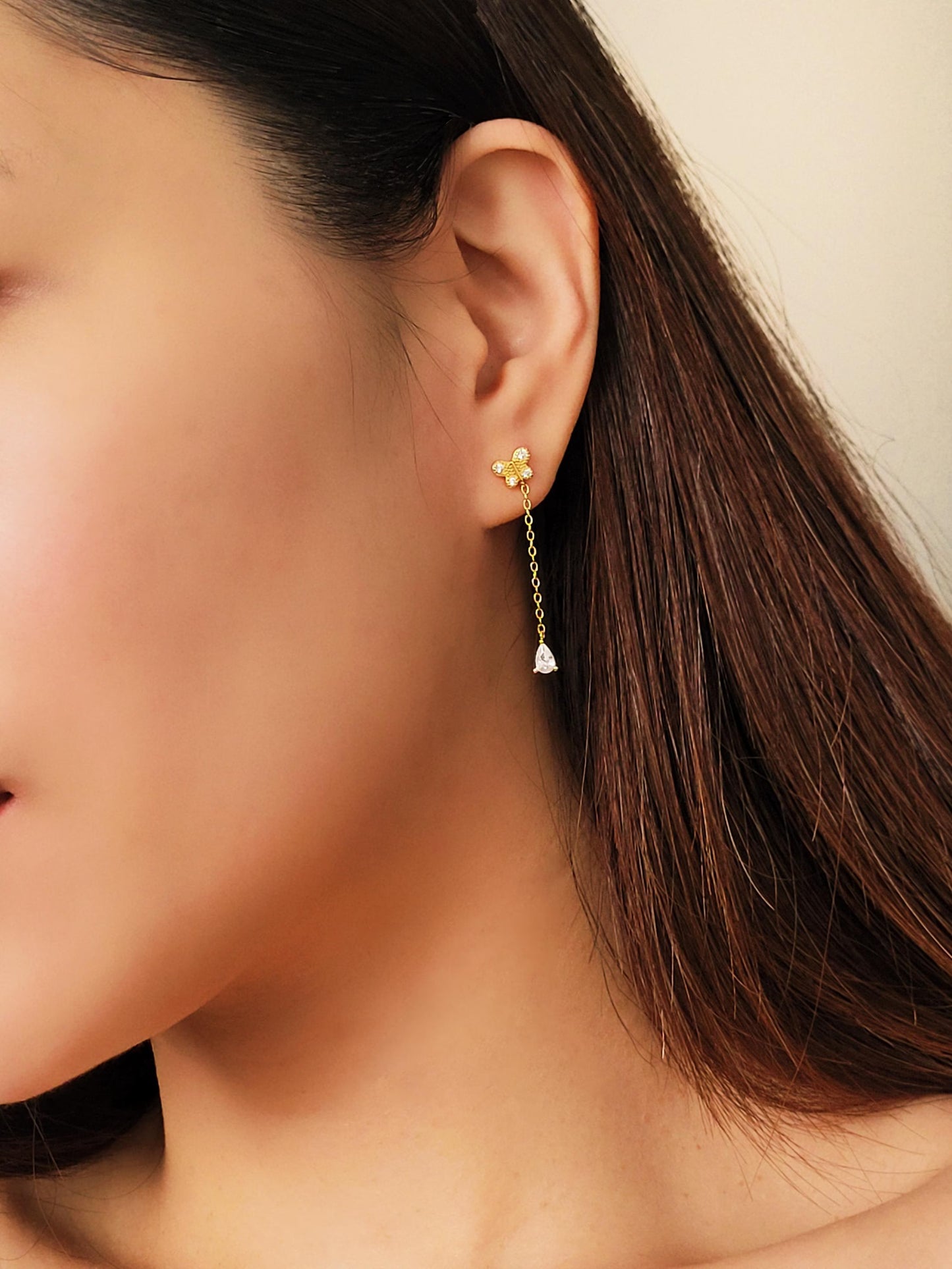 Dainty 18k gold vermeil butterfly stud earring with a delicate chain drop and sparkling pear-cut cubic zirconia stone worn on a model.