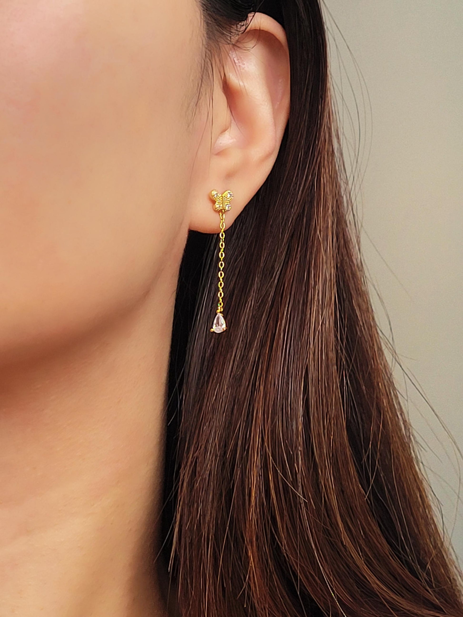 Dainty 18k gold vermeil butterfly stud earring with a delicate chain drop and sparkling pear-cut cubic zirconia stone worn on a model.