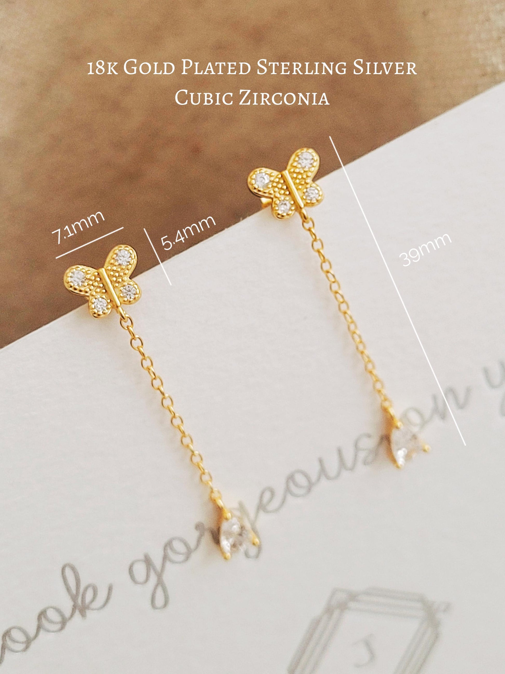 A pair of dainty 18k gold vermeil butterfly stud earring with a delicate chain drop and sparkling pear-cut cubic zirconia stone on a white surface with dimensions.