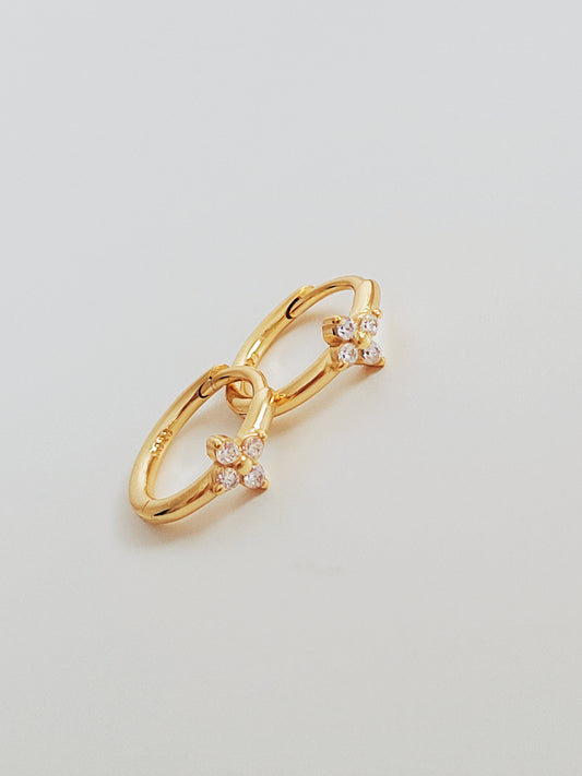 A pair of elegant Gold Clover Huggie Earrings with each earring composed of a small, clover-shaped charm attached to a huggie hoop.