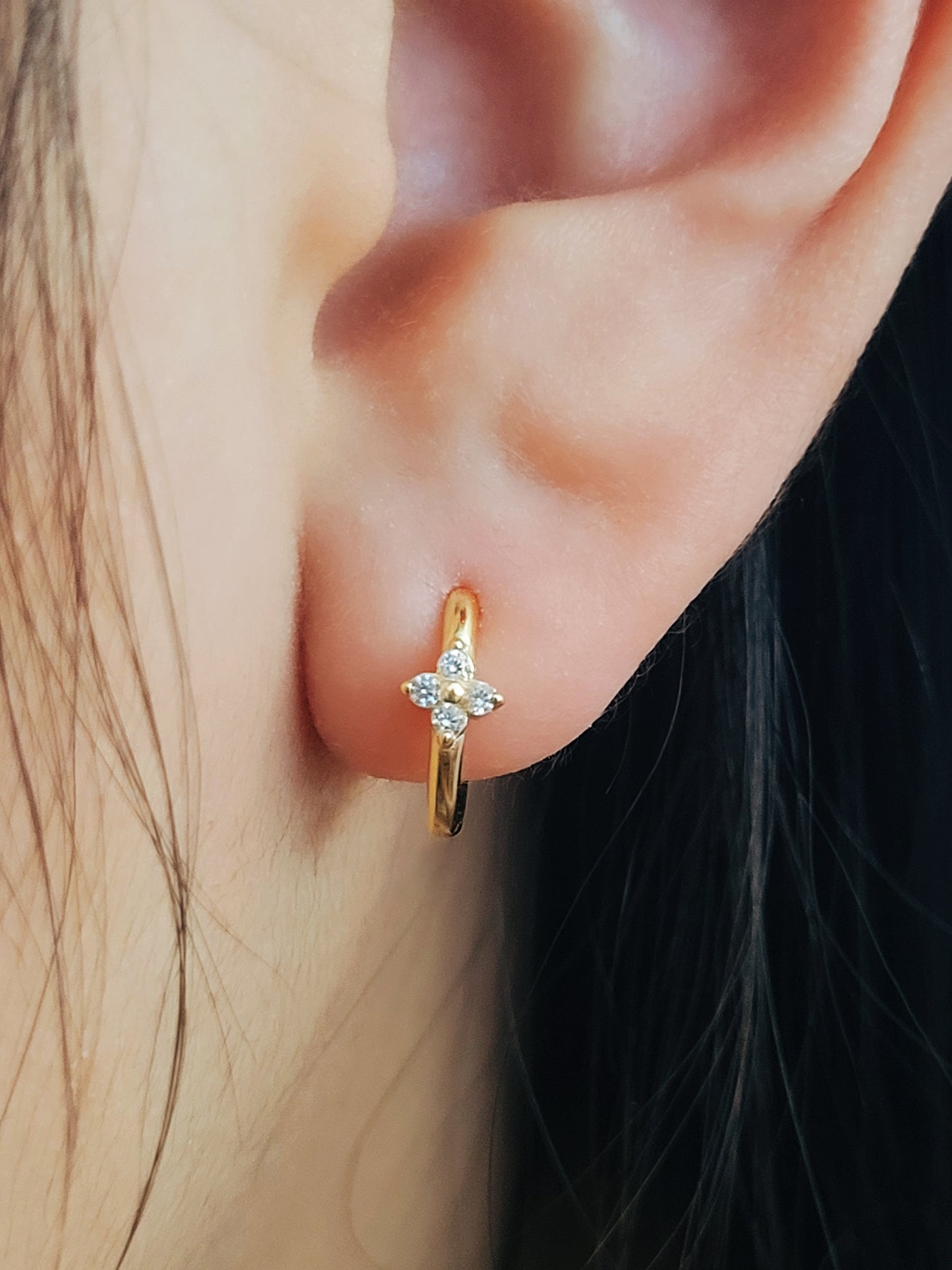A woman wearing gold clover huggie earrings, dainty and minimalist design