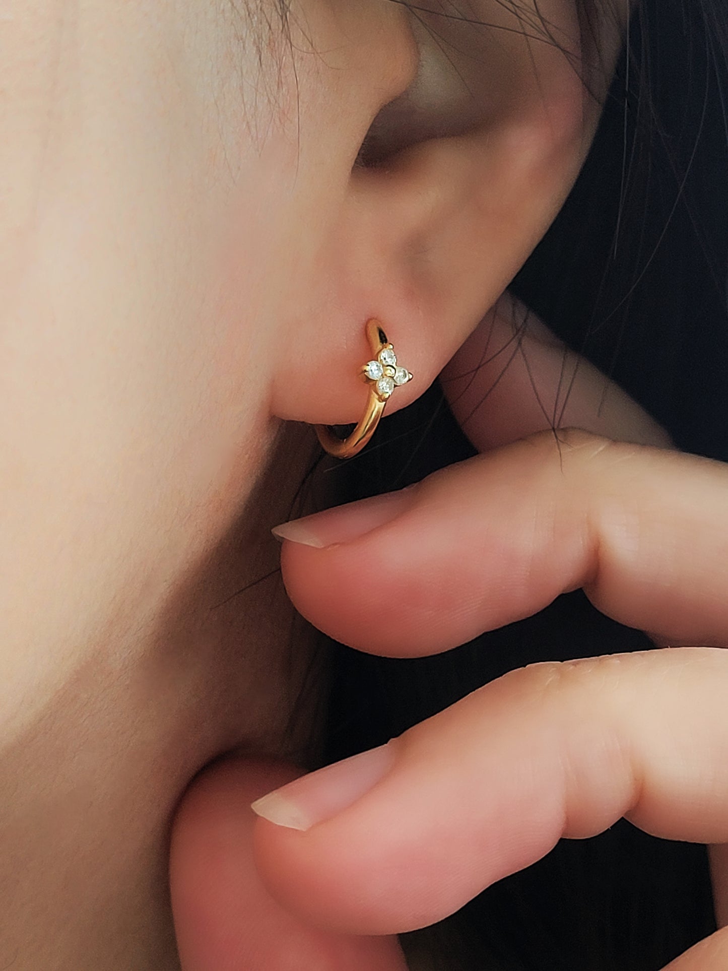 Close up of a lady wearing dainty clover huggie hoop earrings in gold plated sterling silver with shimmering cubic zirconia gemstones.
